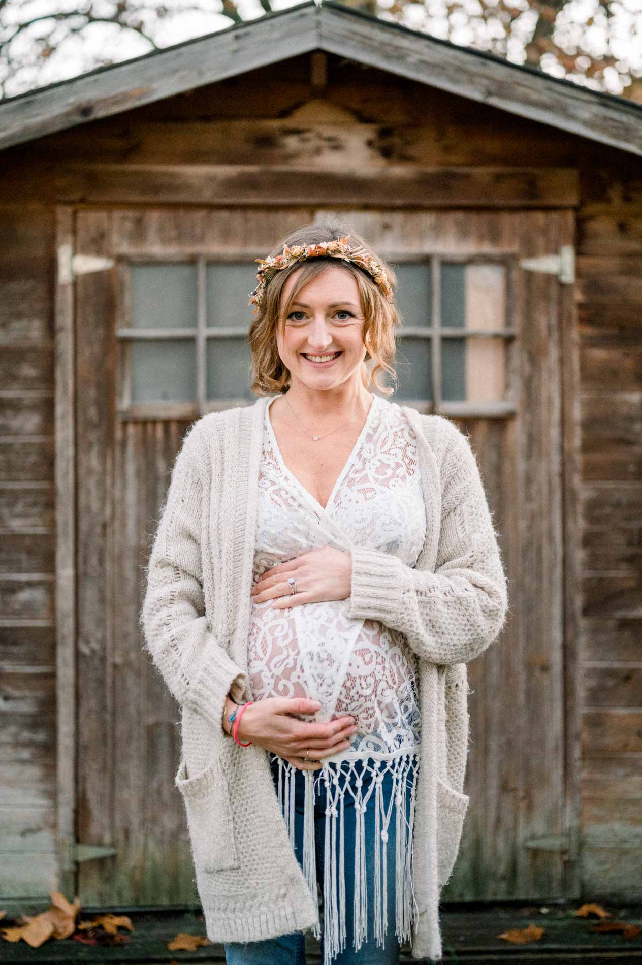Future maman souriante, mains sur le ventre, devant la cabane du jardin