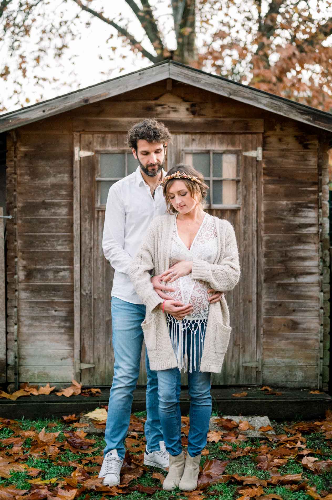 Futurs parents enlacés devant la cabane en bois parmi les feuilles mortes