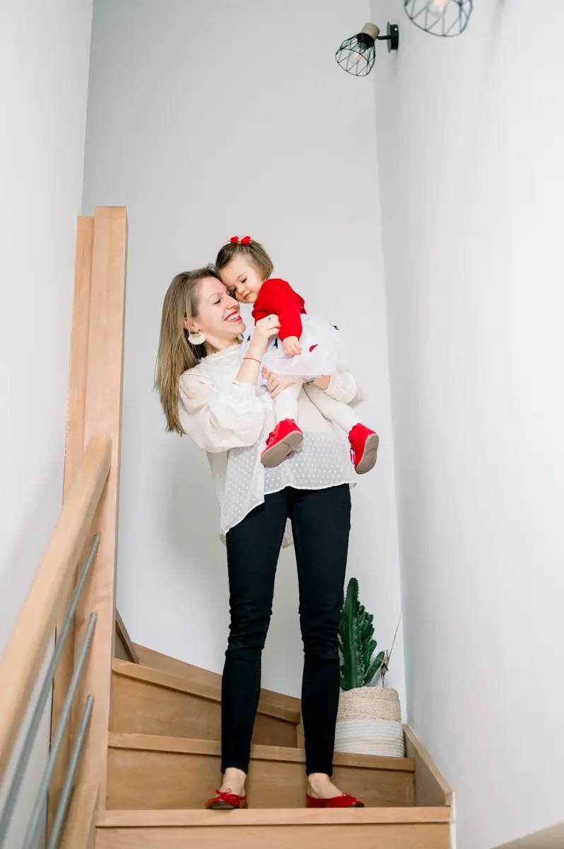 Mother carrying her daughter on the staircase at home, sharing a smile