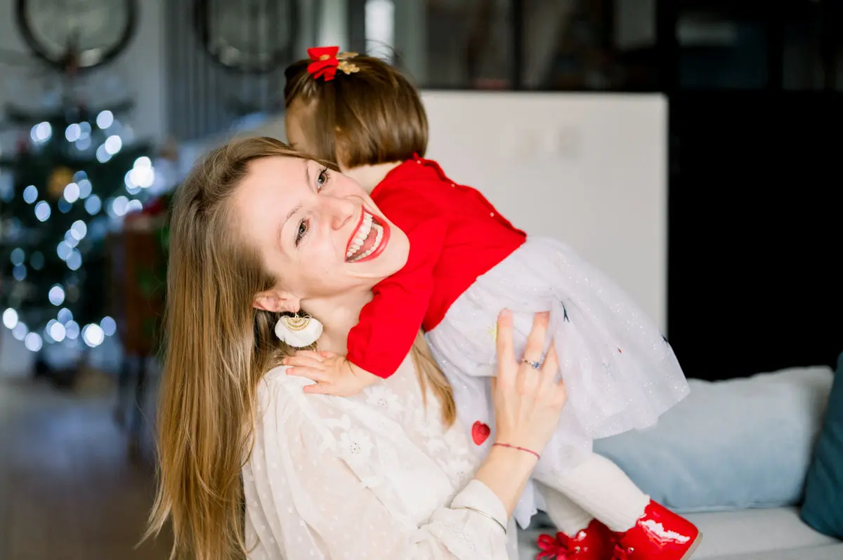 Mother laughing as she hugs her daughter near the Christmas tree