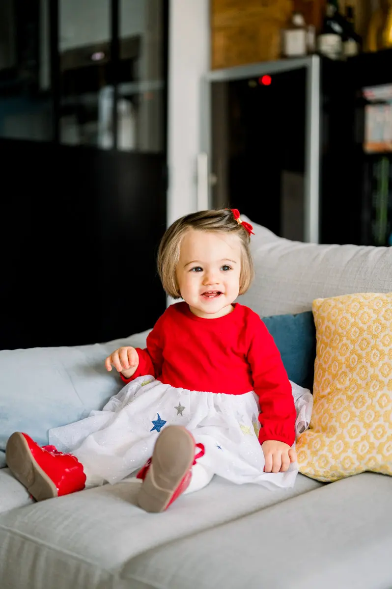 Smiling little girl sitting on the grey sofa in red and white