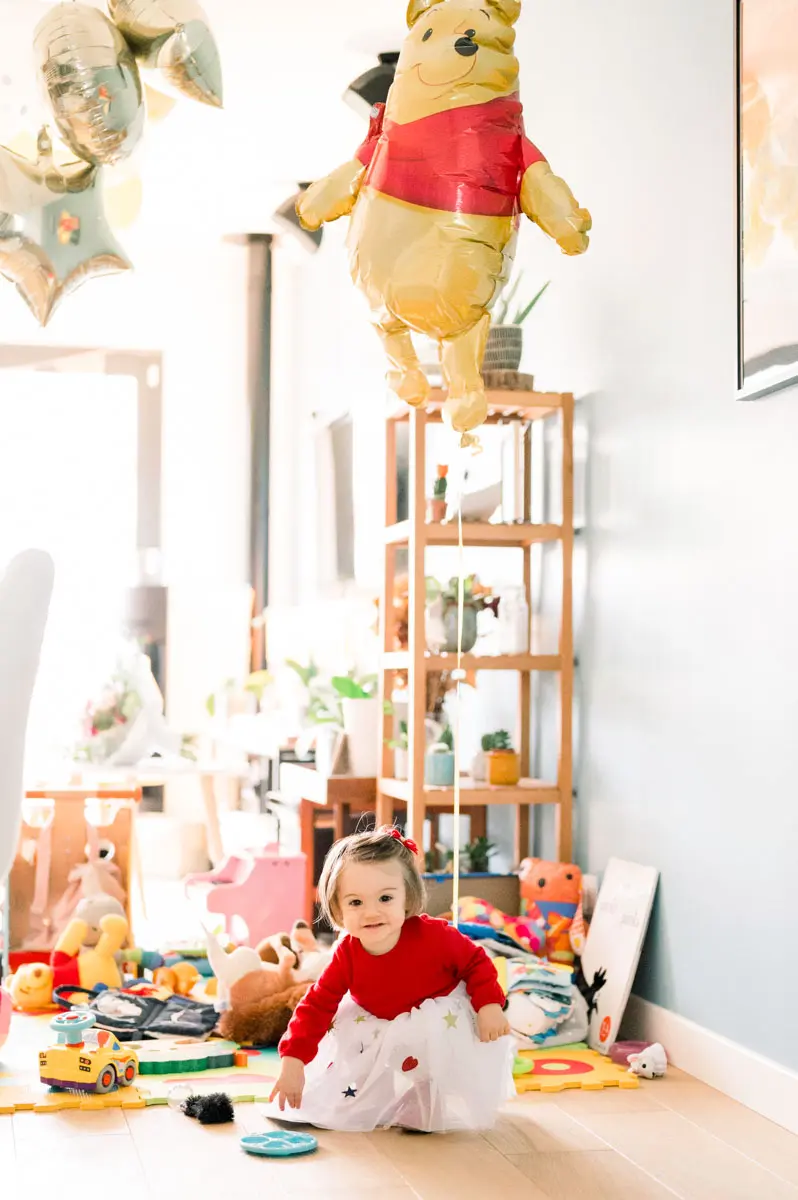 Little girl playing among her toys beneath a Winnie the Pooh balloon
