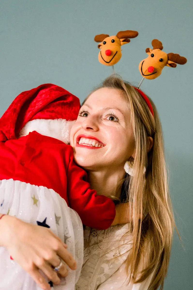 Mother in a reindeer headband hugging her daughter in a Santa hat