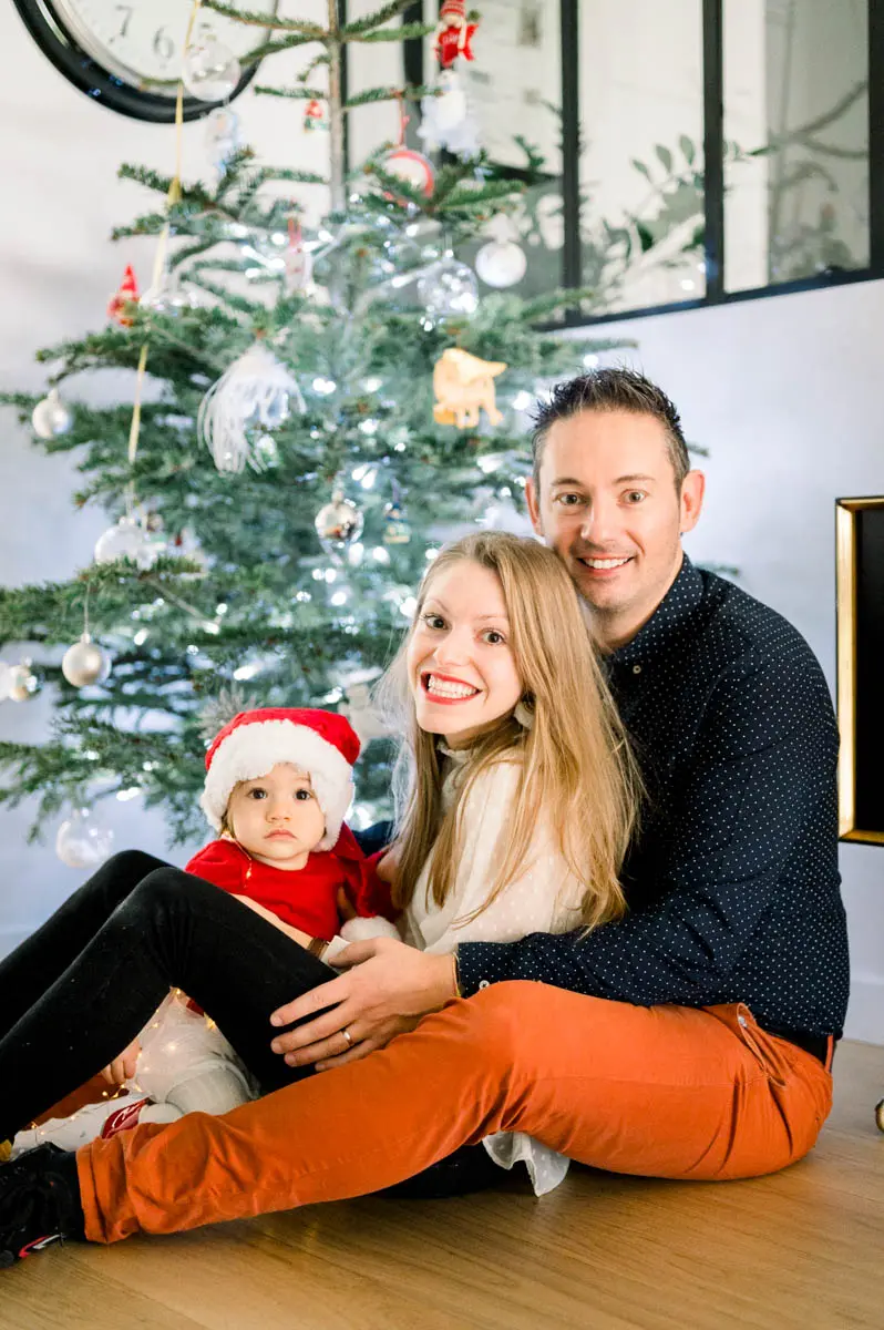 Family sitting at the foot of the Christmas tree, baby in a red hat