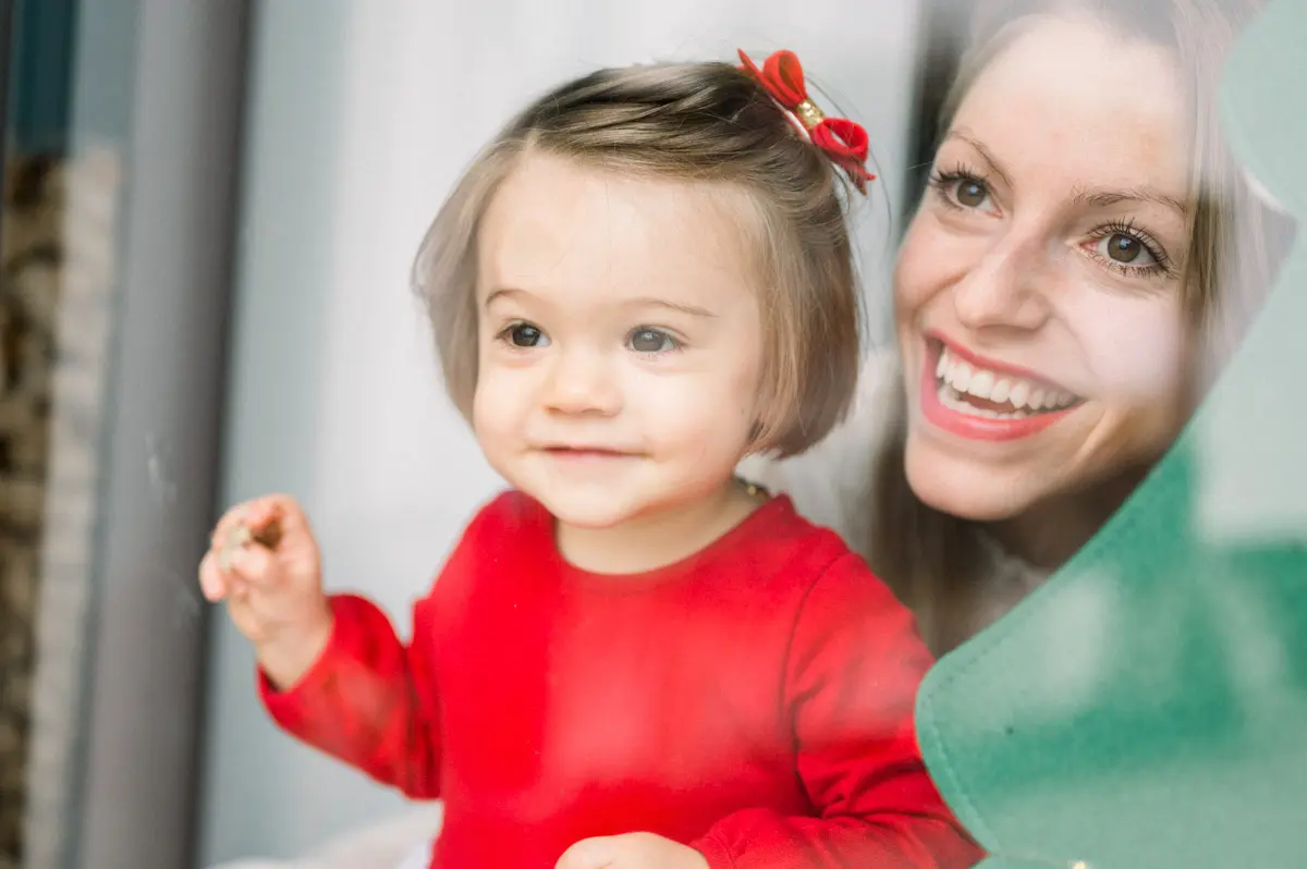 Smiling little girl in her mother's arms by the window