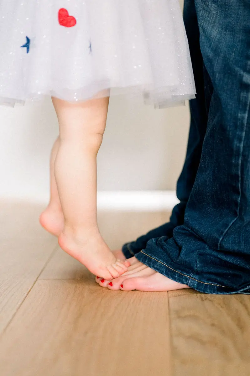 Little girl's bare feet standing on her father's feet