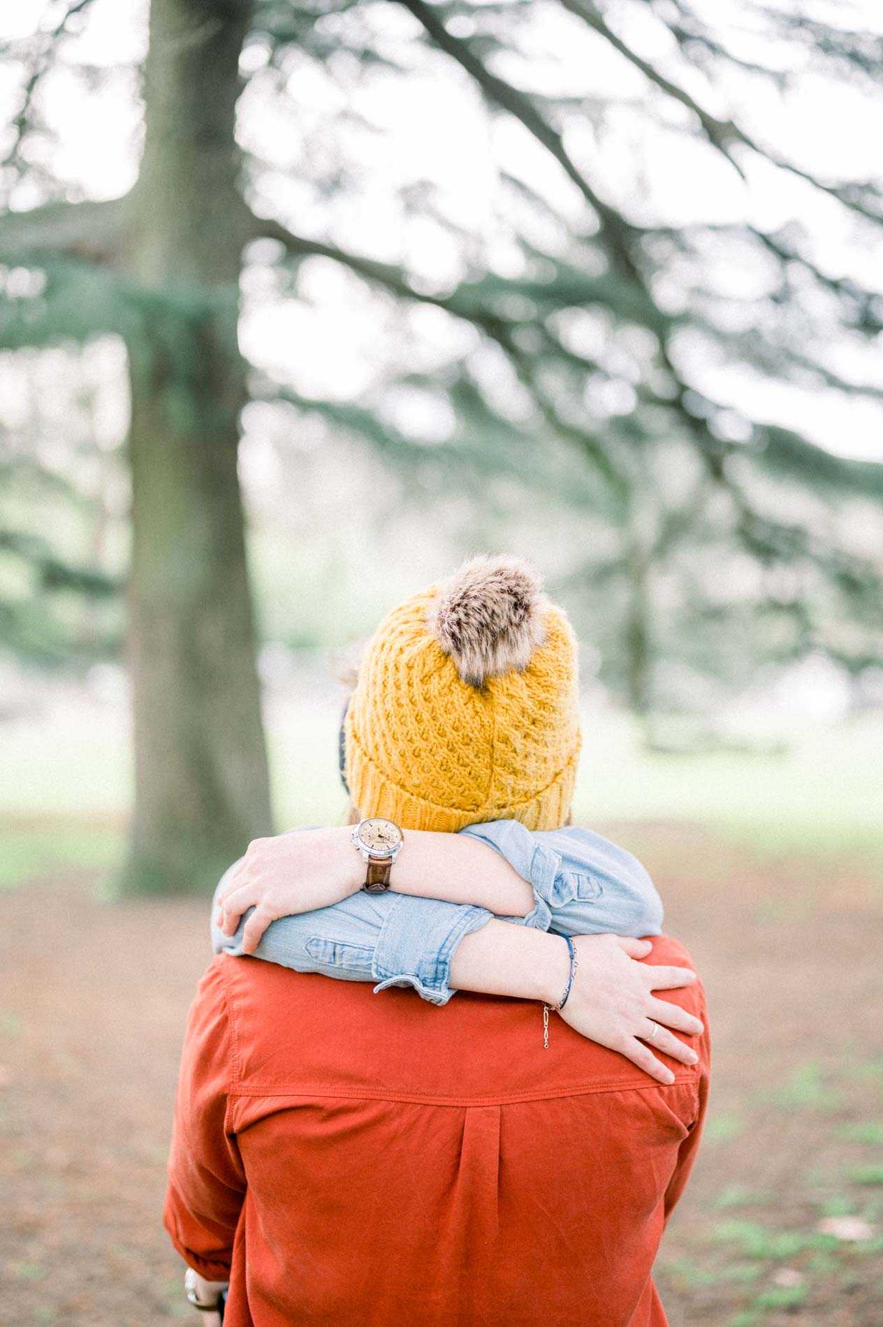 Two women embracing beneath a large cedar, seen from behind