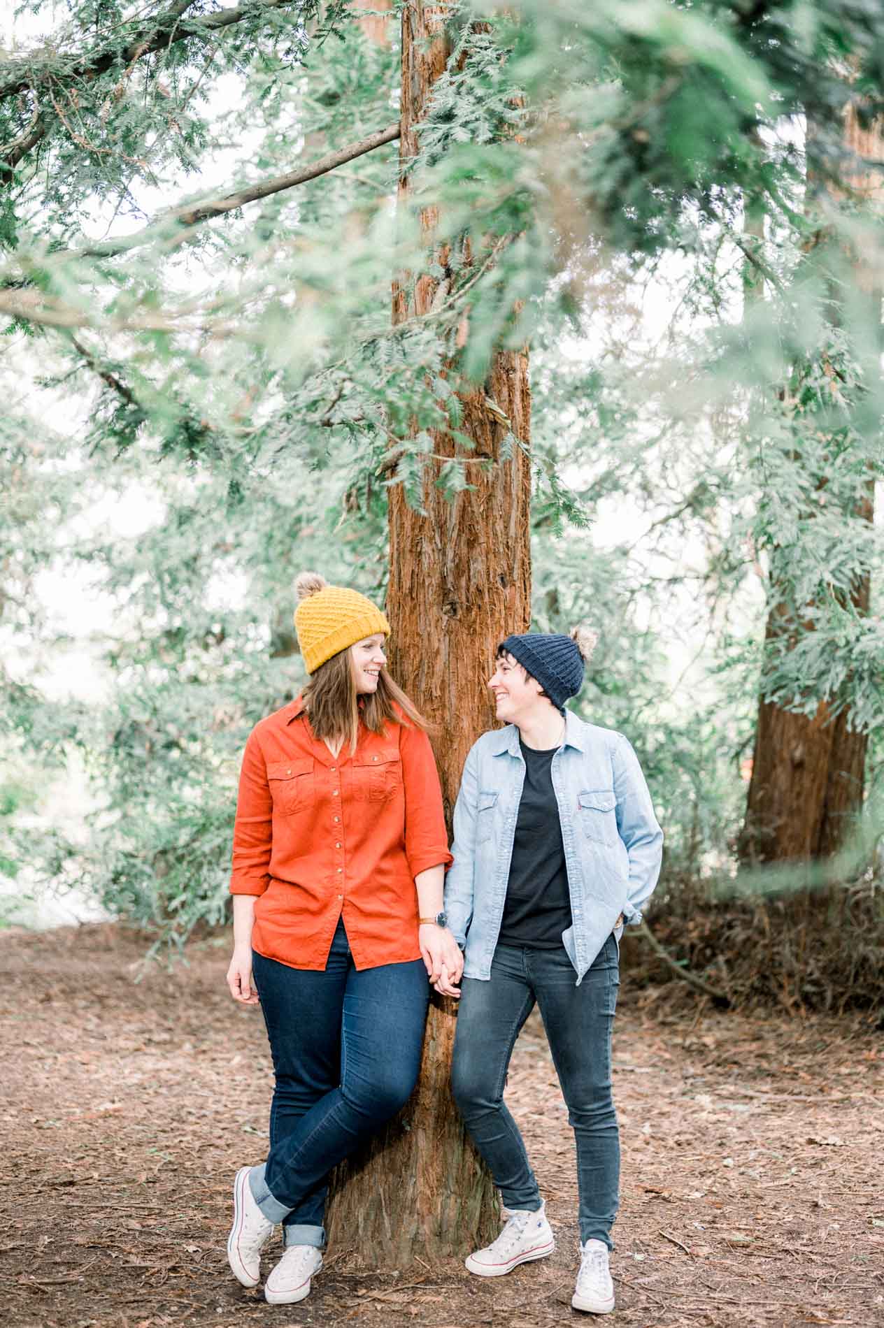 The couple leaning against a redwood trunk, hand in hand