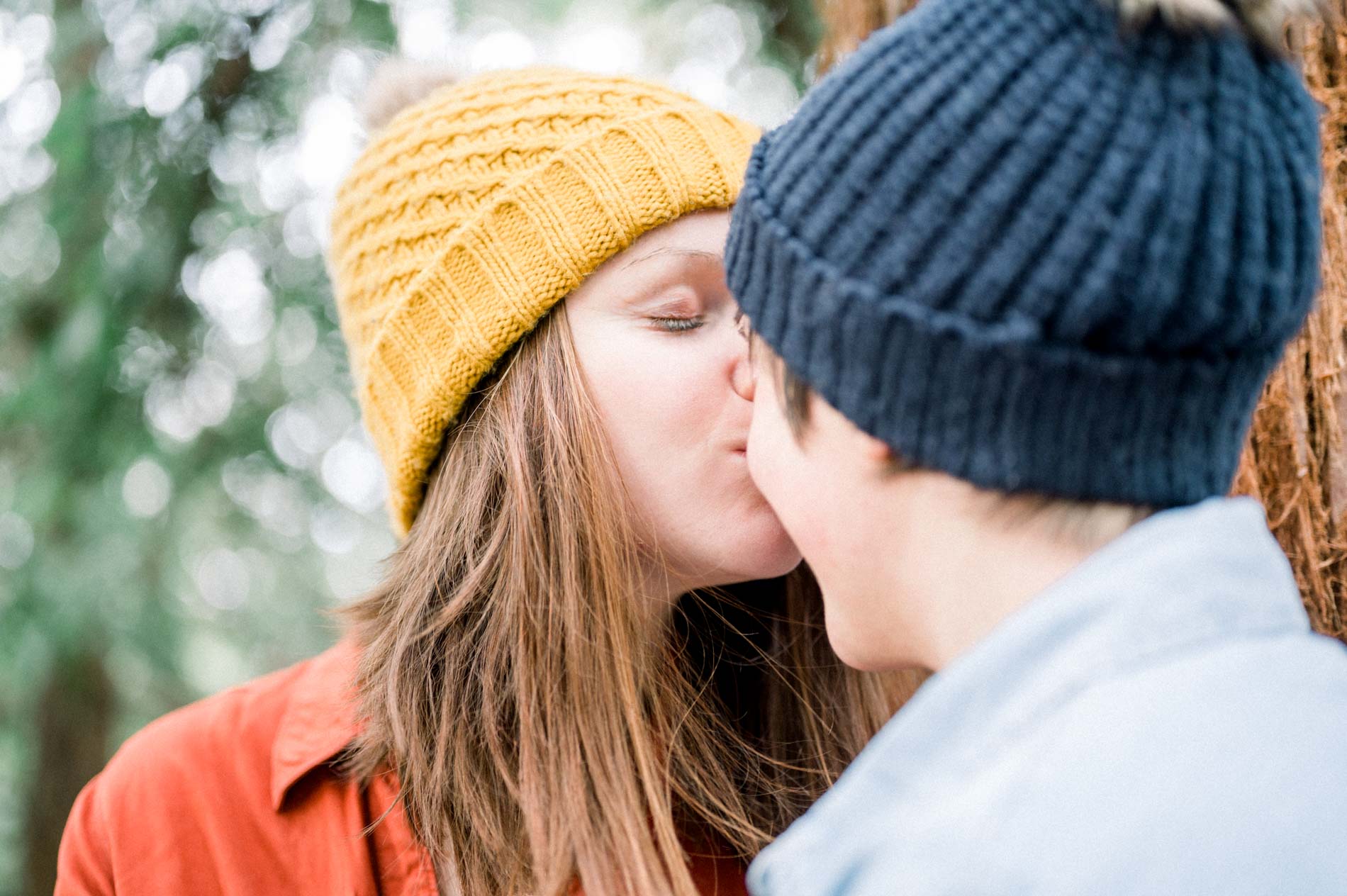 Tender kiss between two women in mustard and navy beanies