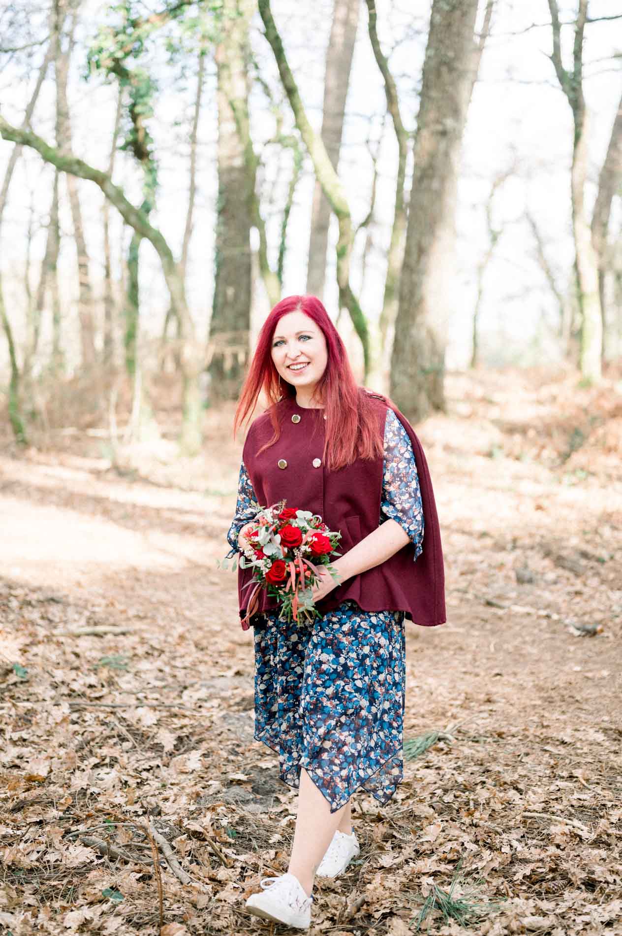 Red-haired woman holding a bouquet of red roses on a forest path