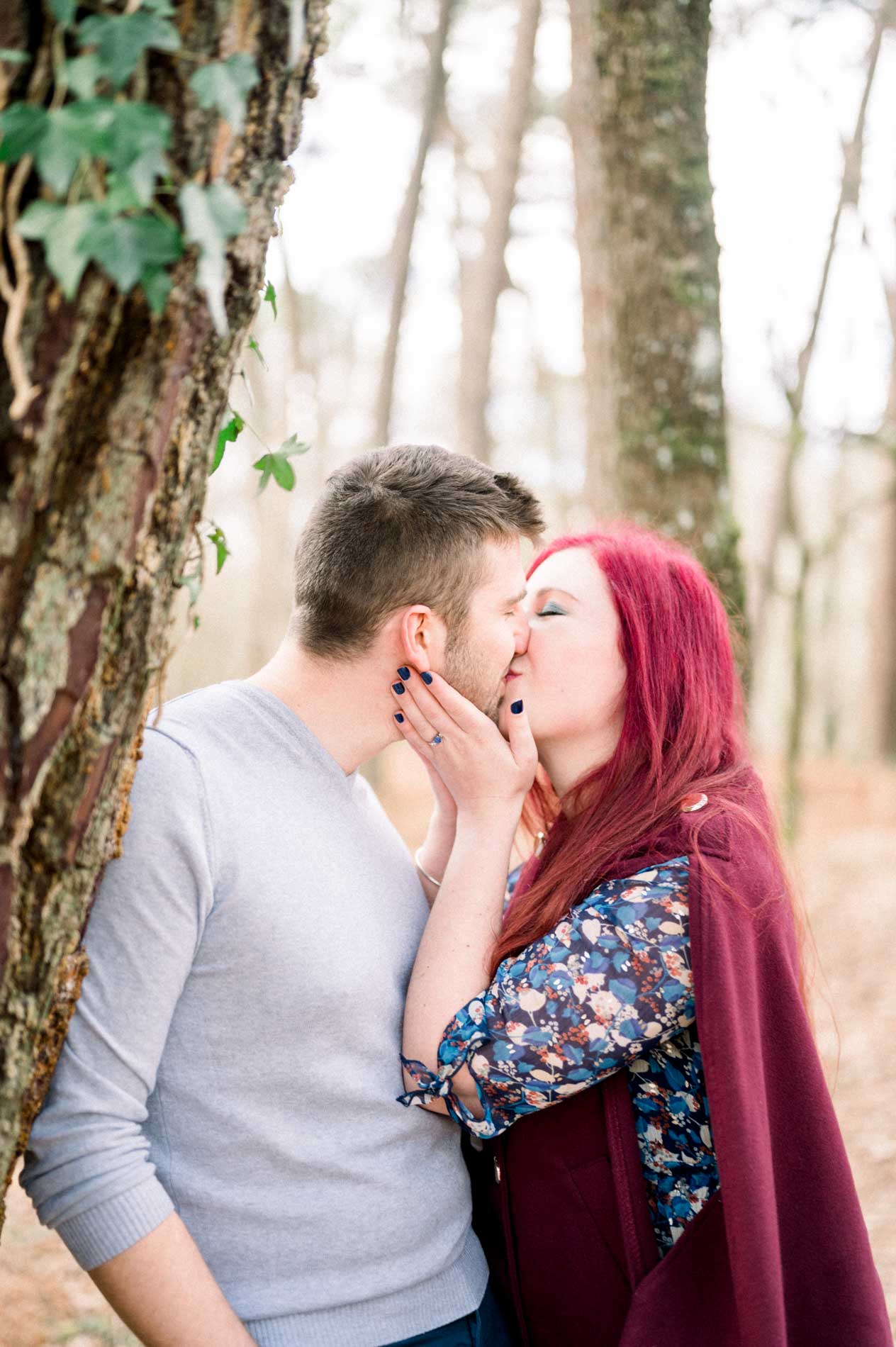 Couple kissing against an ivy-covered trunk during the engagement shoot