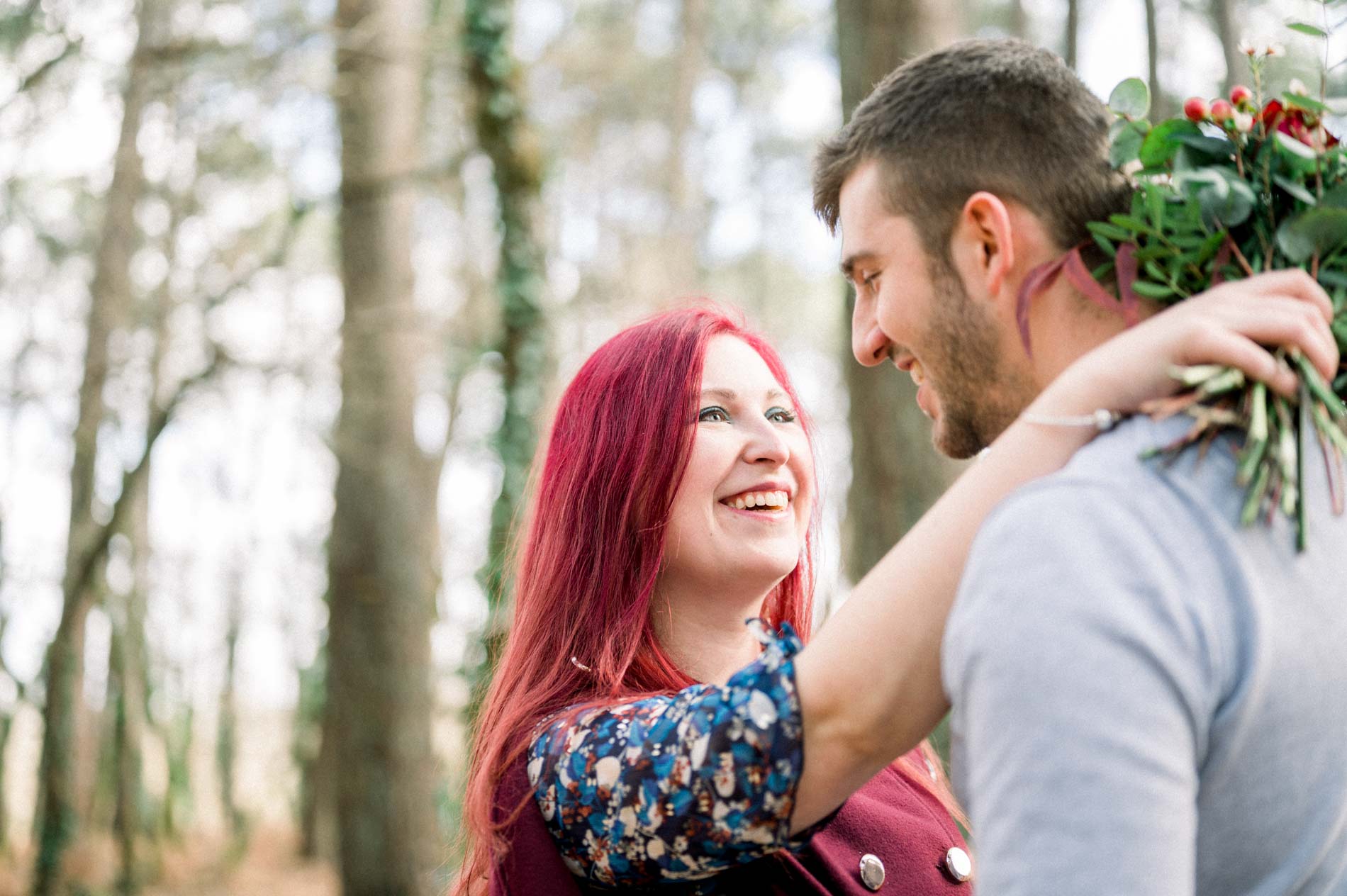 Playful couple in the woods, bouquet of roses resting on his shoulder