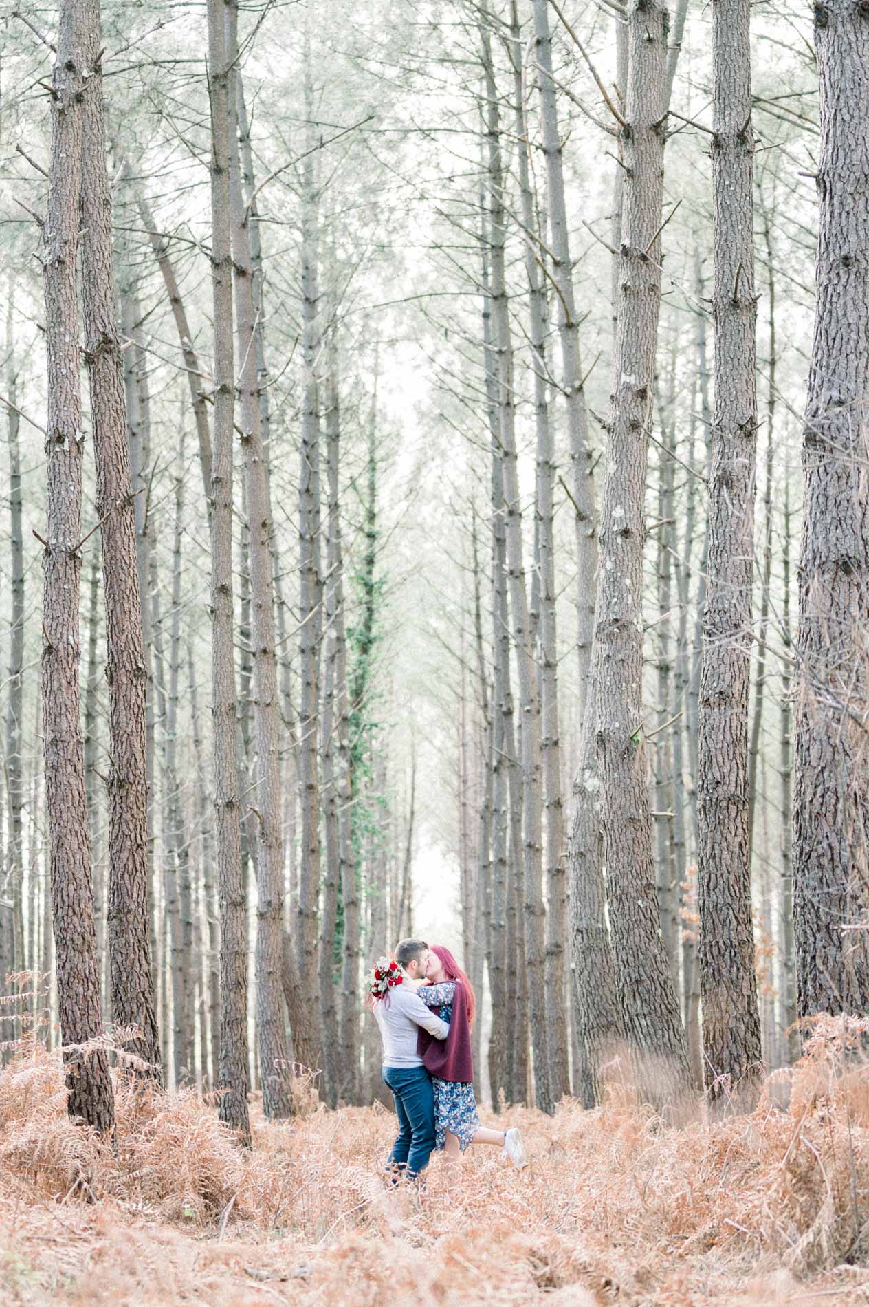 Couple embracing at the foot of slender pines, dry ferns in the foreground