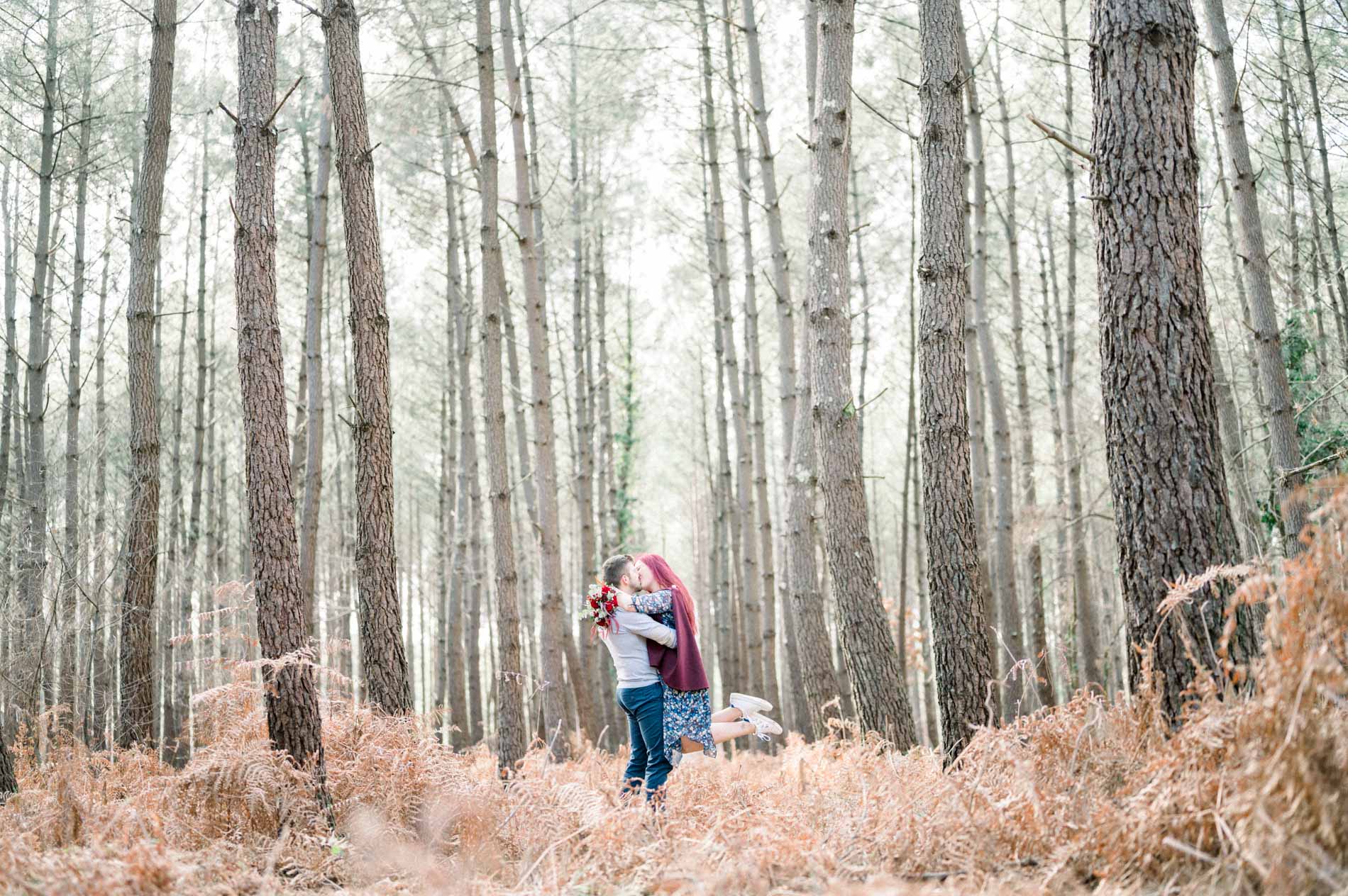 Couple embracing among tall pines in a winter forest, engagement session