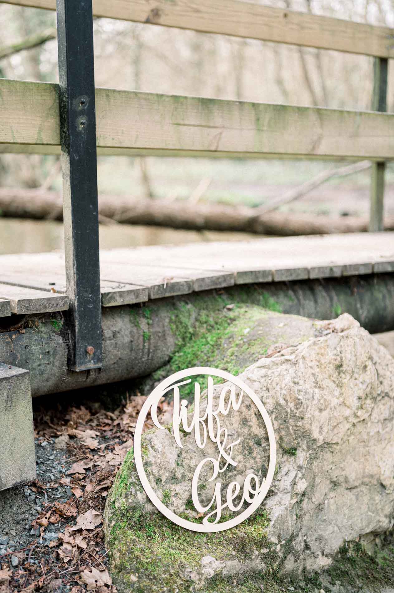 Engraved wooden sign on a mossy rock at the foot of a footbridge