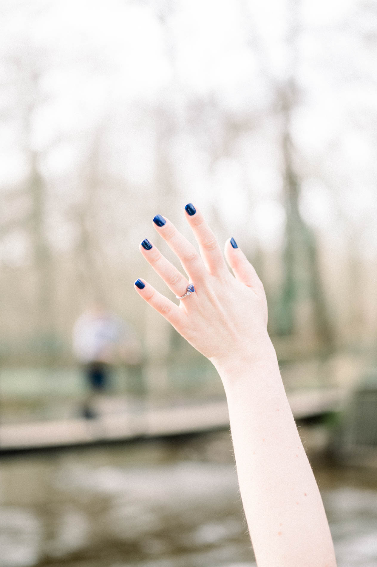 Raised hand showing the engagement ring, man blurred on the footbridge