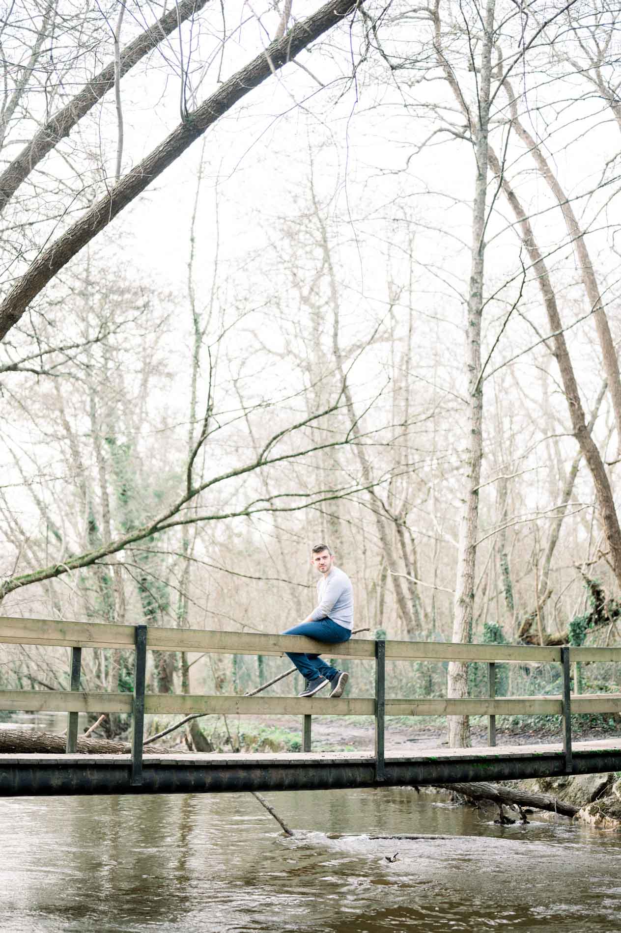 Man sitting on a wooden footbridge over a forest stream