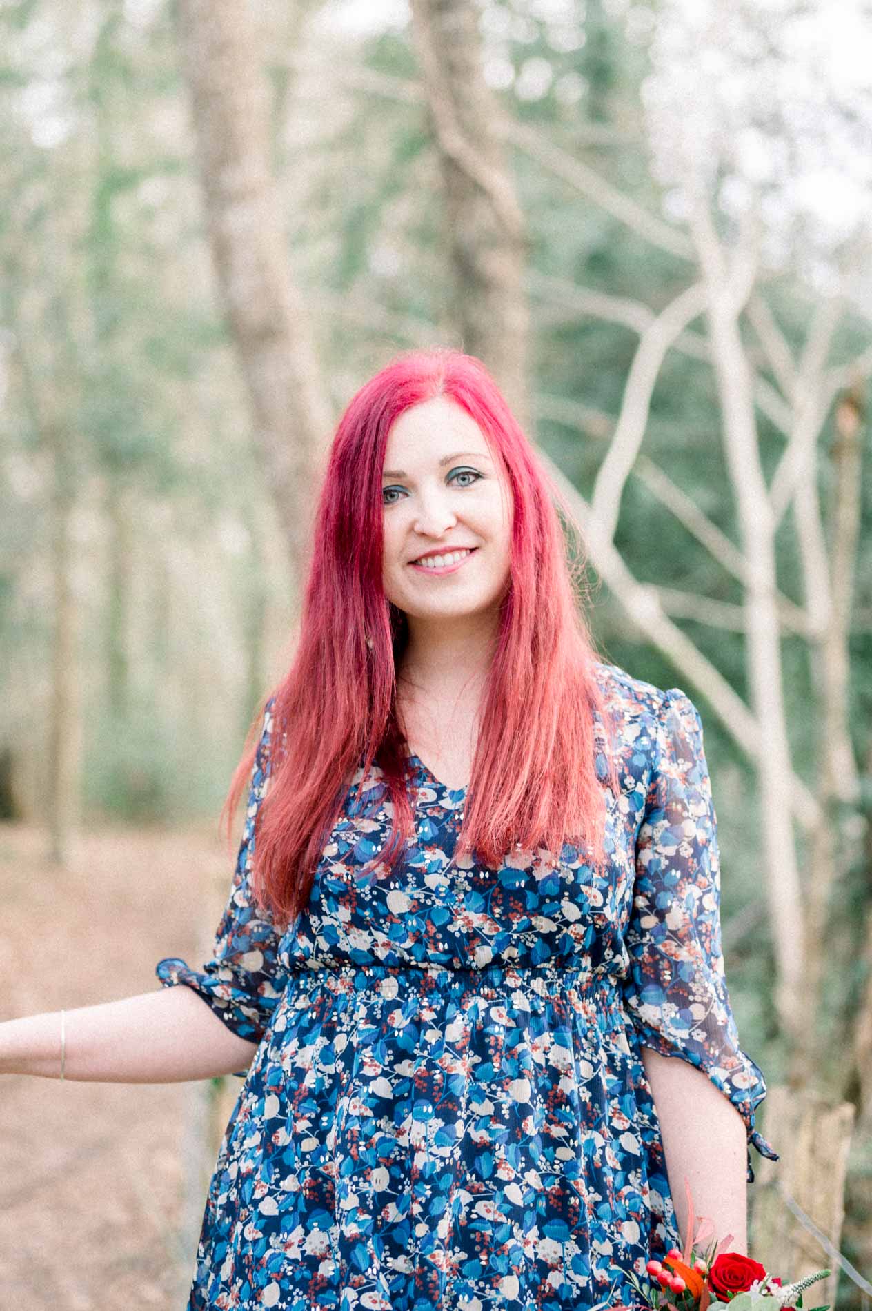 Red-haired woman in a floral dress smiling among the trees