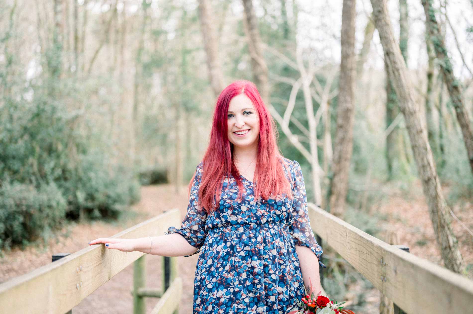Smiling woman leaning on the railing of a forest footbridge
