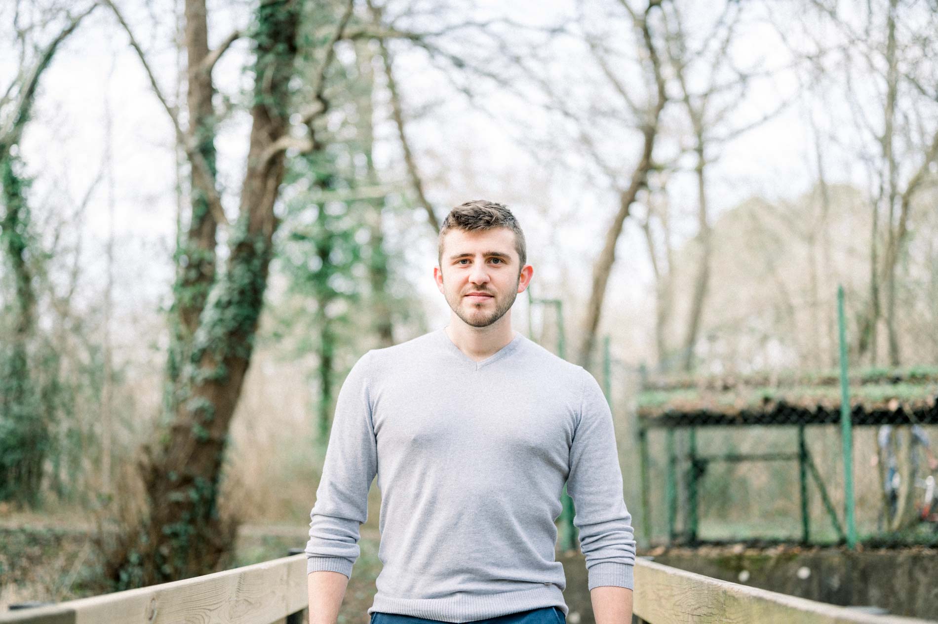 Man in a grey jumper smiling on a wooden footbridge