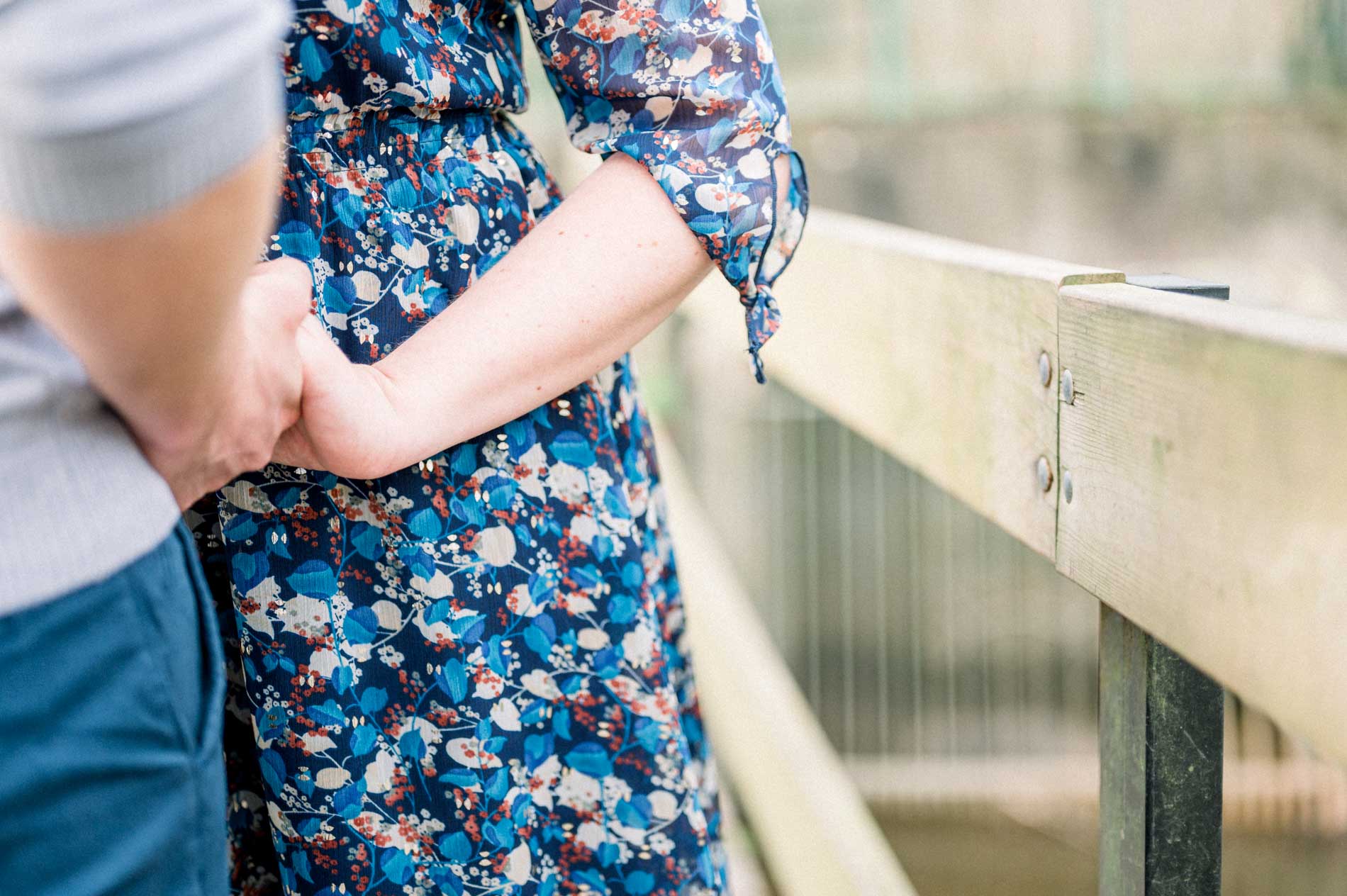 Couple's hands intertwined by the railing of a footbridge
