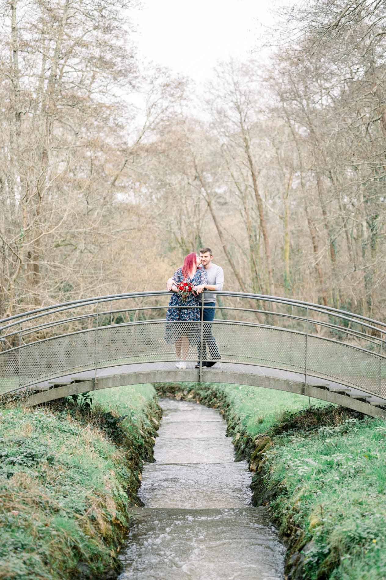Couple embracing on a small stone bridge over a green stream