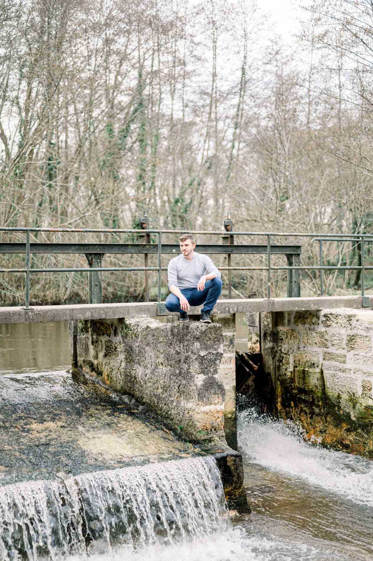 Man crouching on an old stone weir above a small waterfall