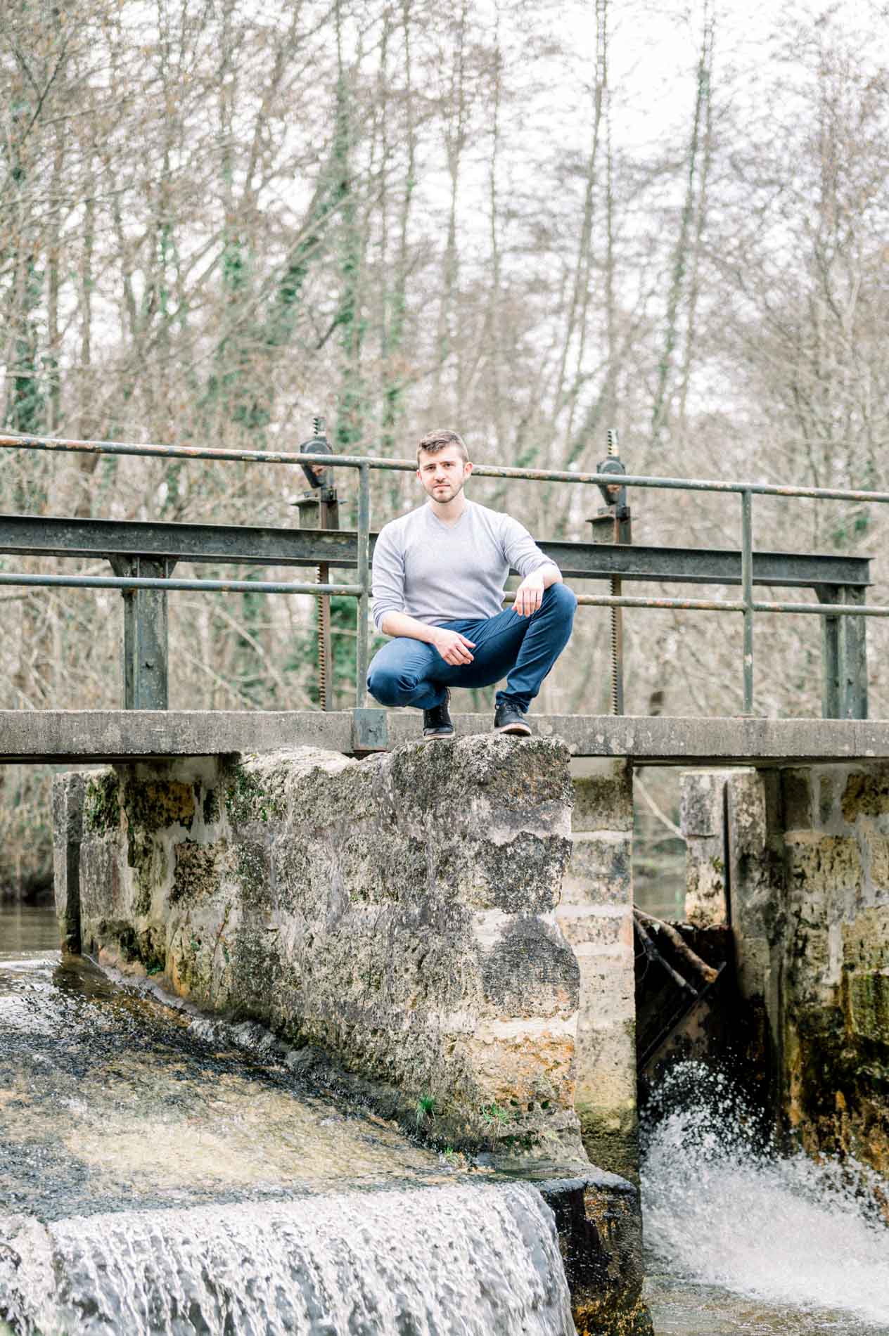 Man in a grey jumper crouching on the weir, waterfall in the foreground