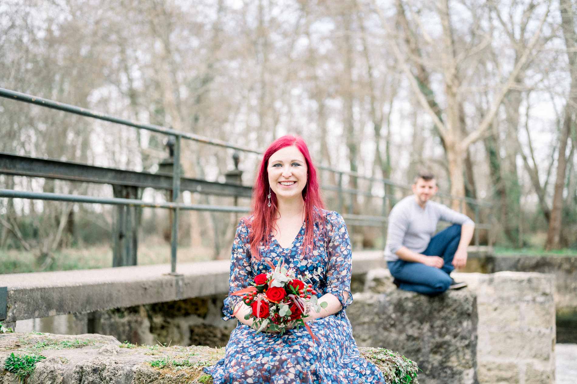 Smiling woman with her rose bouquet, partner seated on the weir