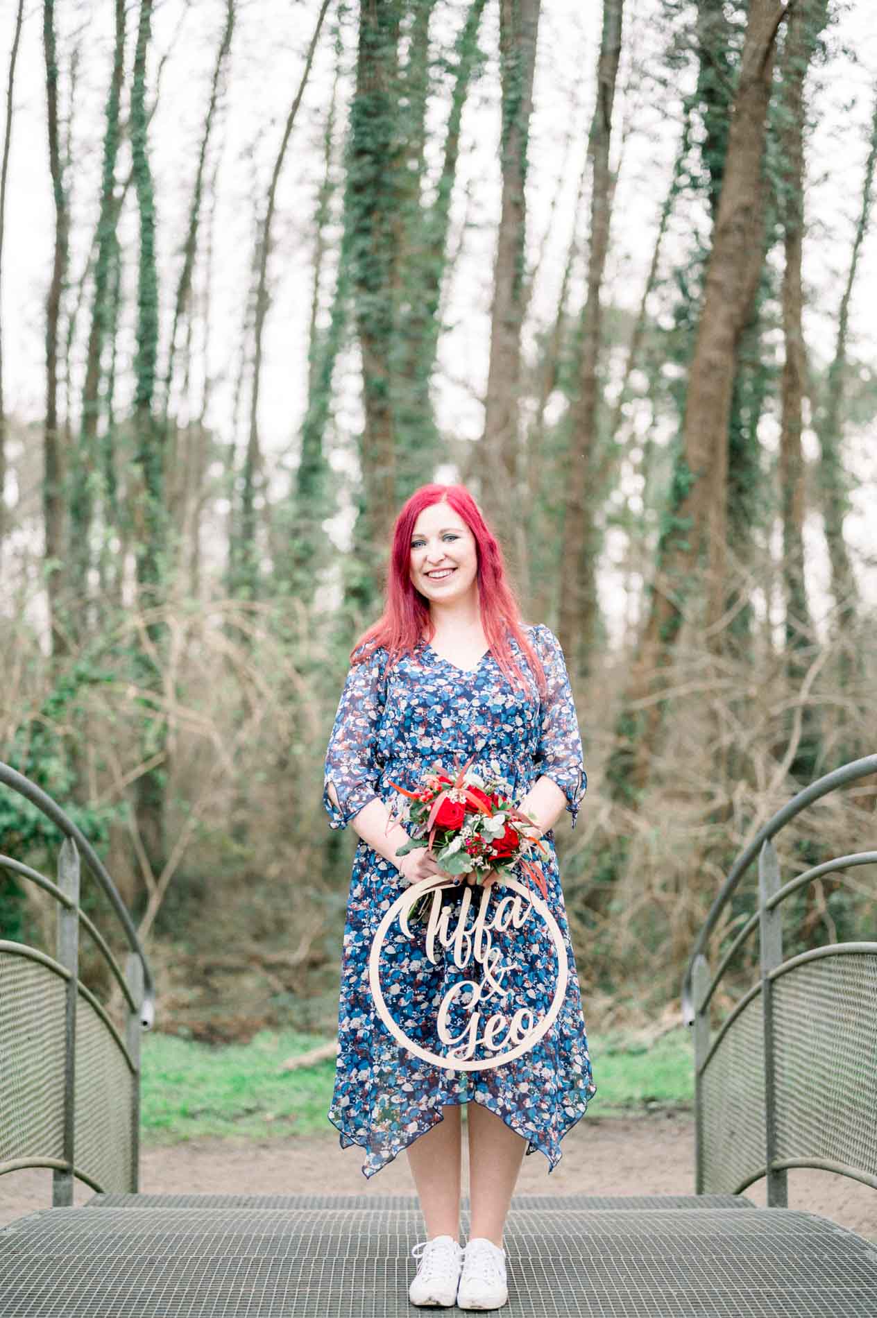 Woman holding a bouquet and wooden sign on a forest footbridge