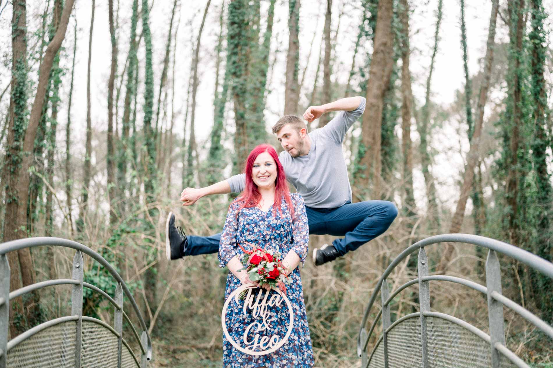 Man leaping behind his partner as she holds the bouquet and sign
