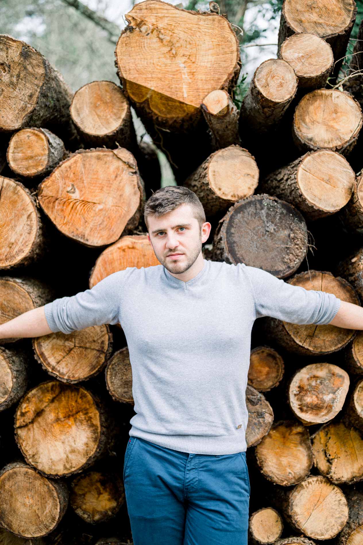 Man with arms outstretched in front of a log pile in the forest