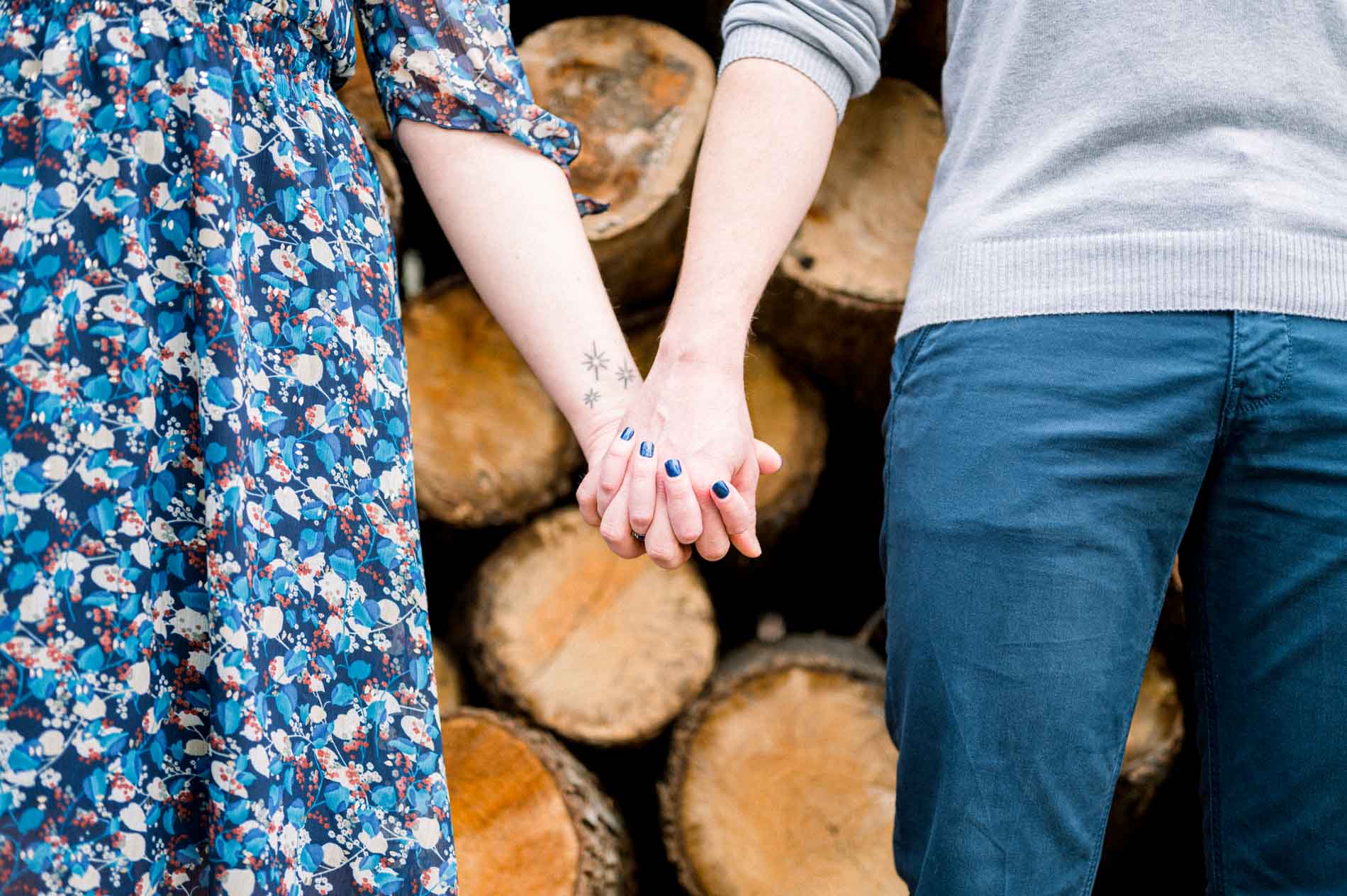 Couple's joined hands in front of a pile of logs