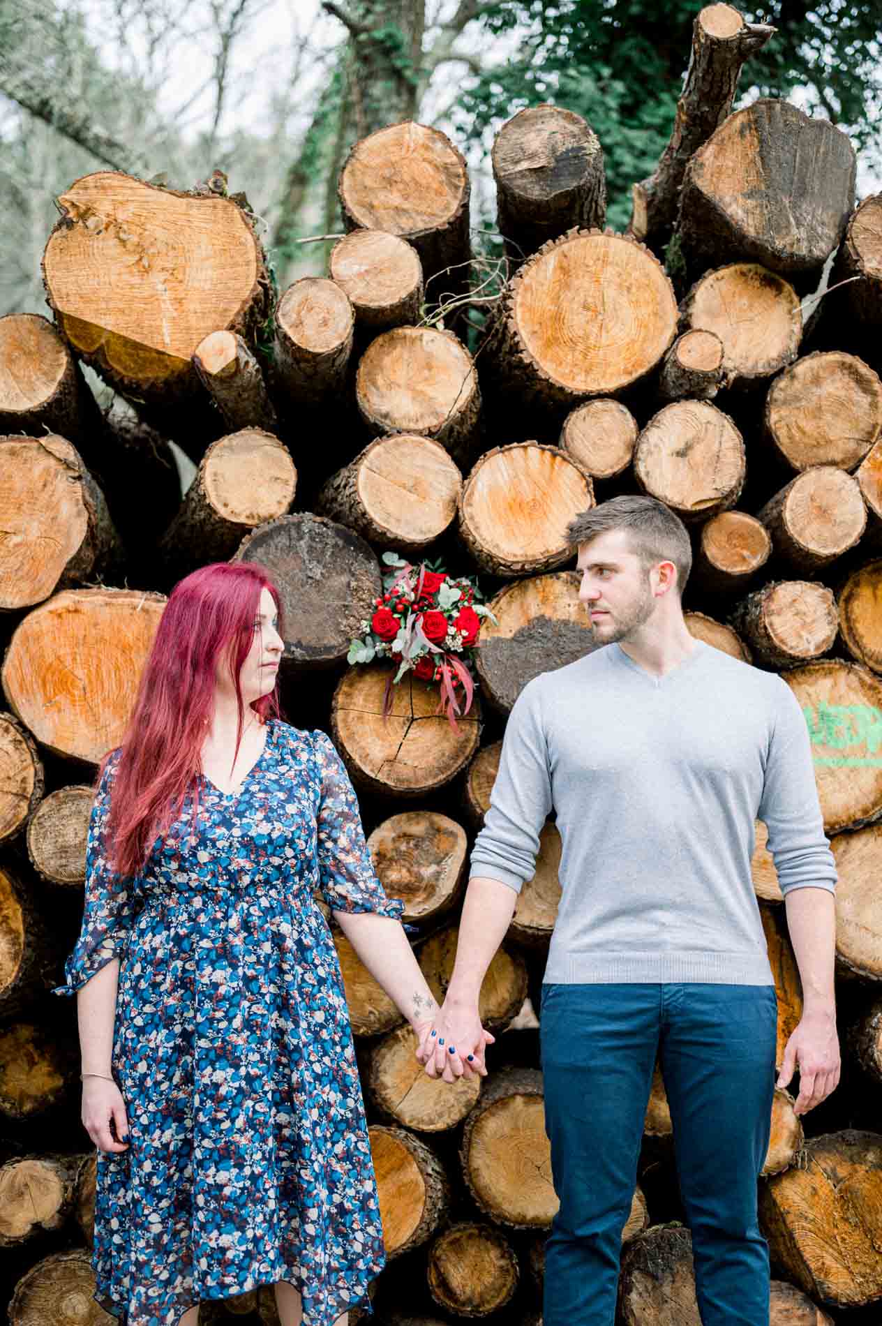 Couple holding hands in front of a woodpile, sharing a look