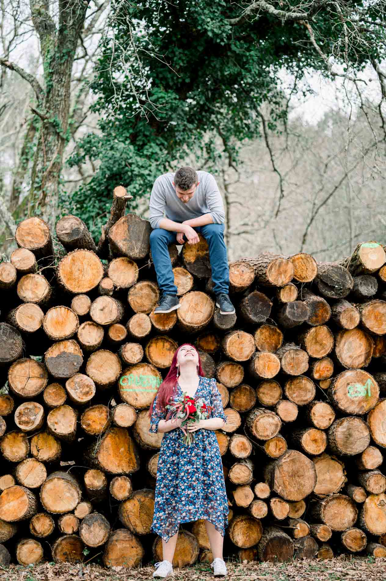 Man sitting on the woodpile, his partner standing below with her bouquet