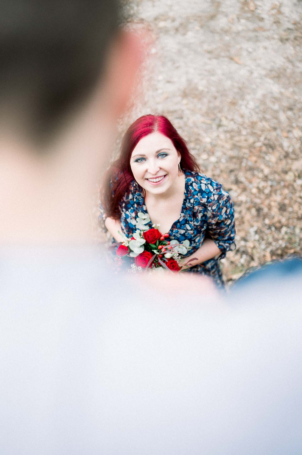 Woman crouching with her bouquet among fallen leaves, looking up at her partner