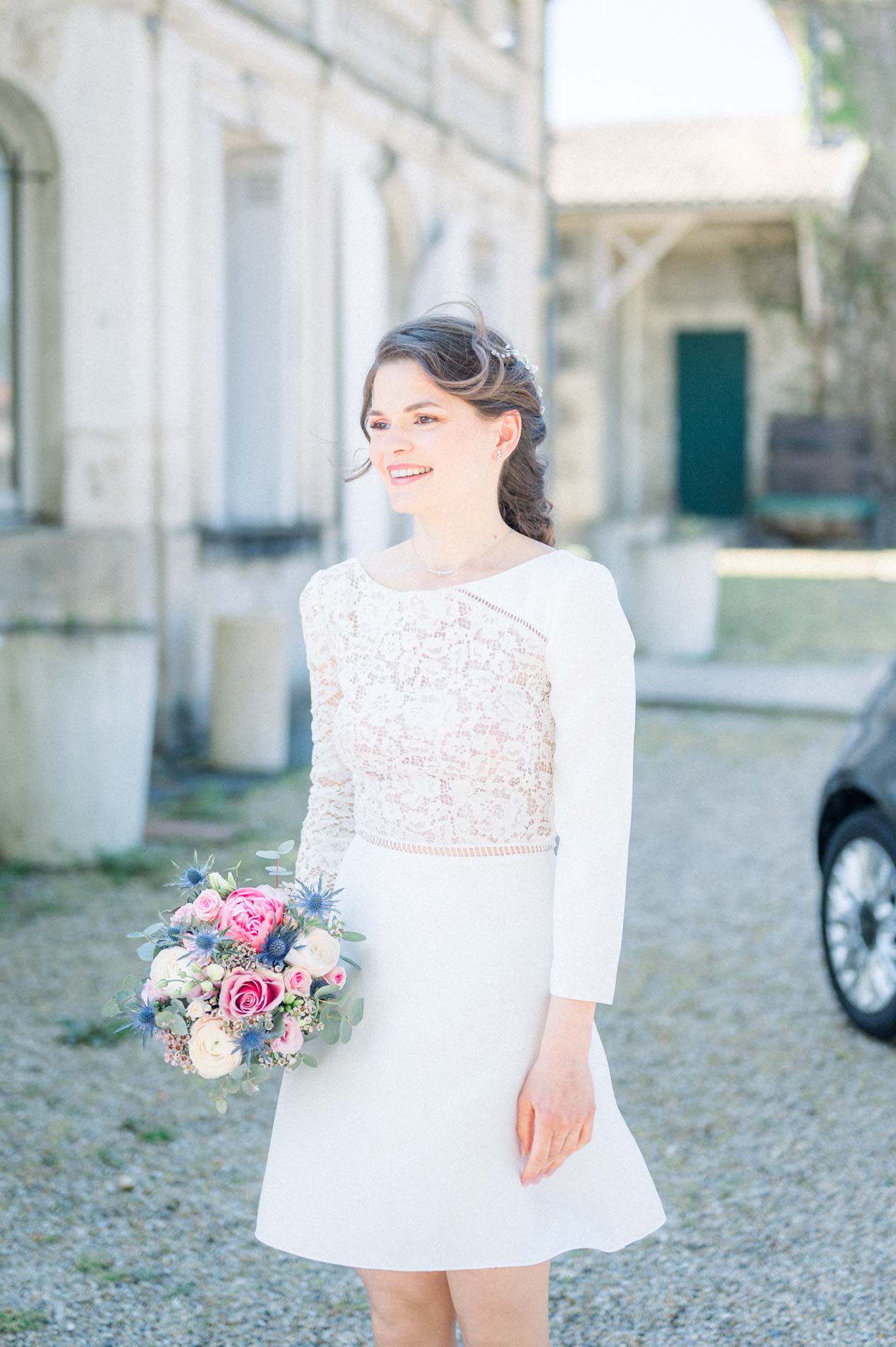 La mariée en robe courte et top en dentelle tient son bouquet pastel