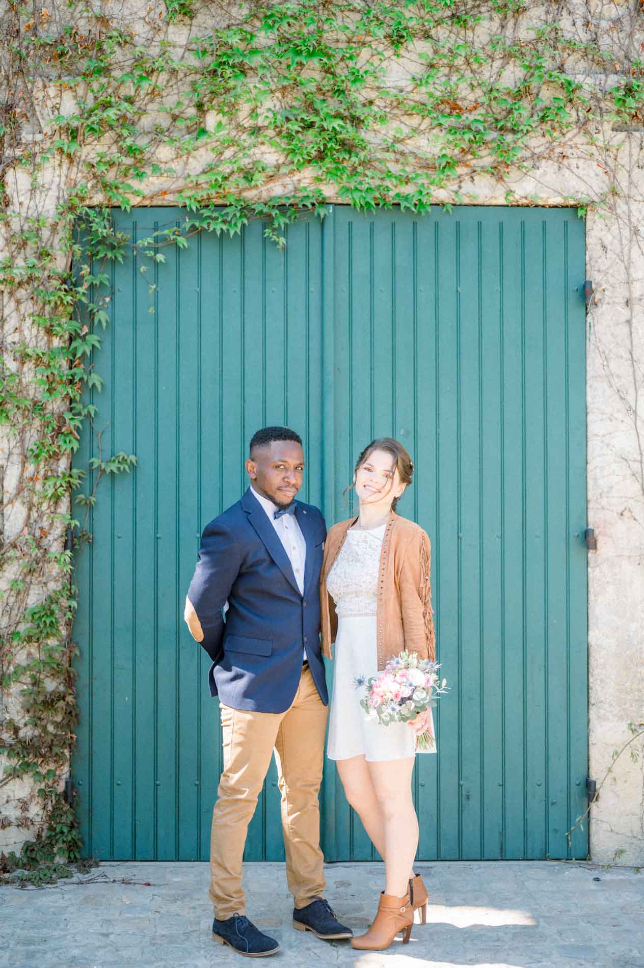 Les mariés posent devant une grande porte en bois verte couverte de lierre