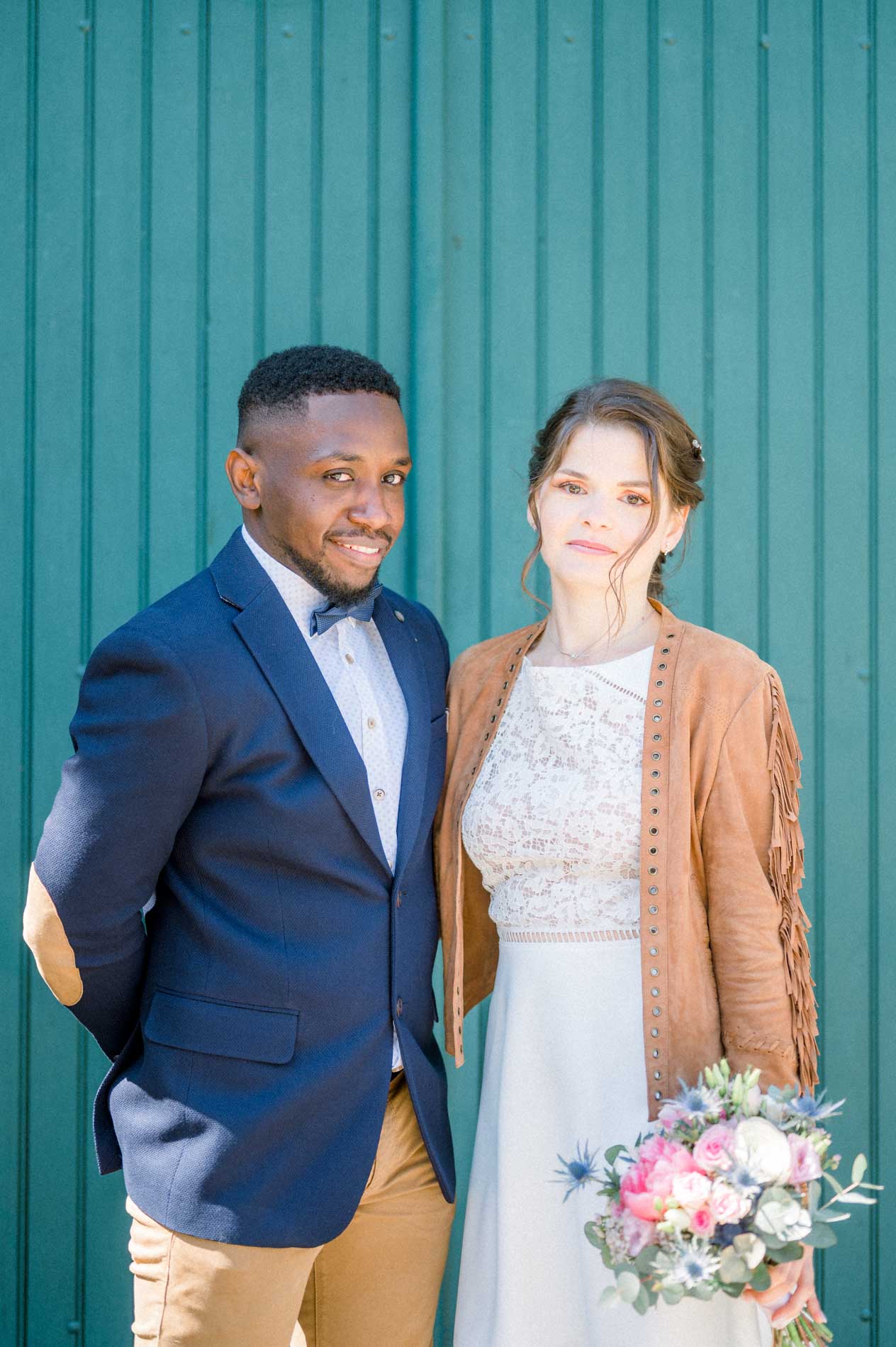 Le marié en blazer bleu et la mariée en veste à franges, porte verte
