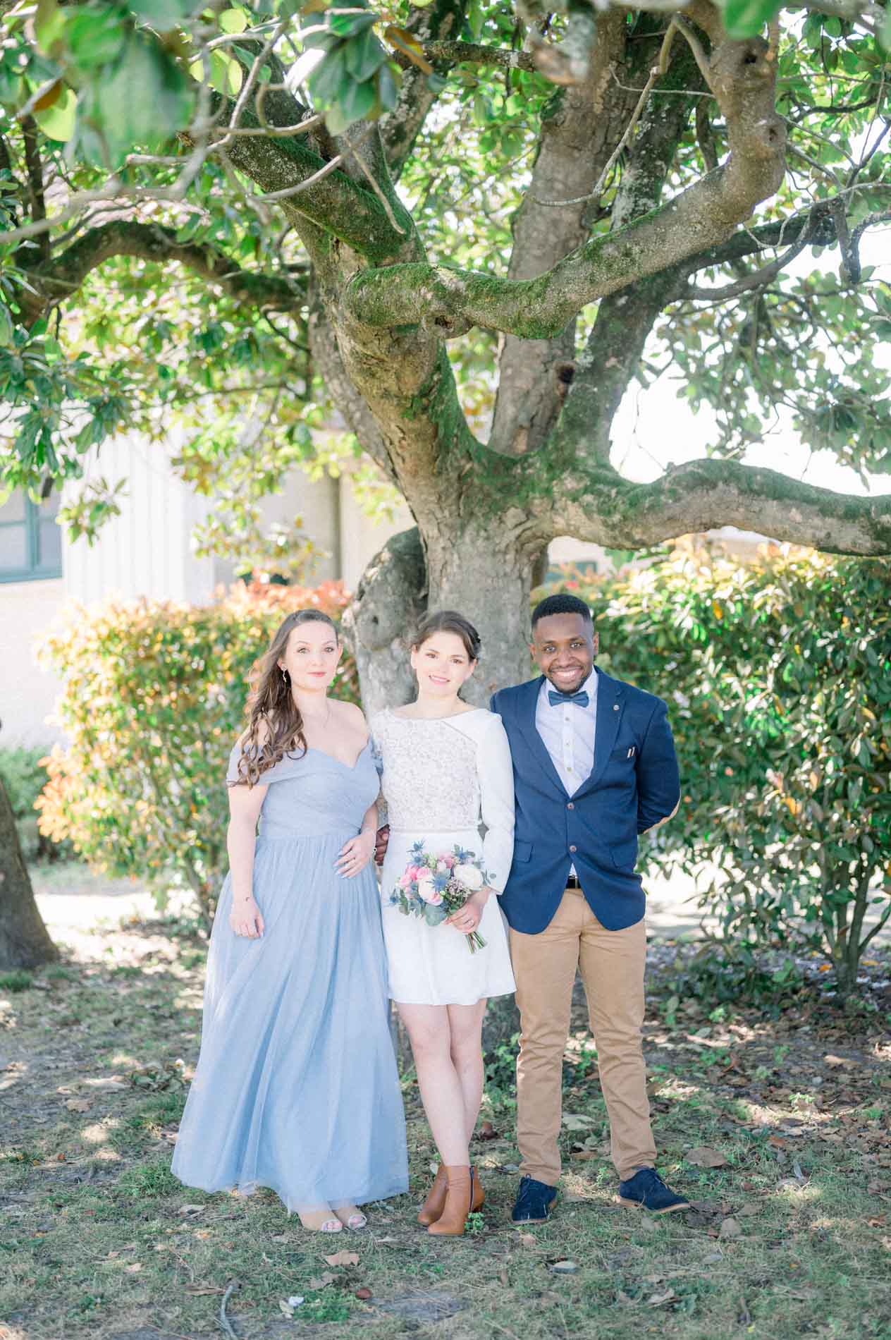 Les mariés et leur témoin en robe bleue sous un grand arbre du domaine