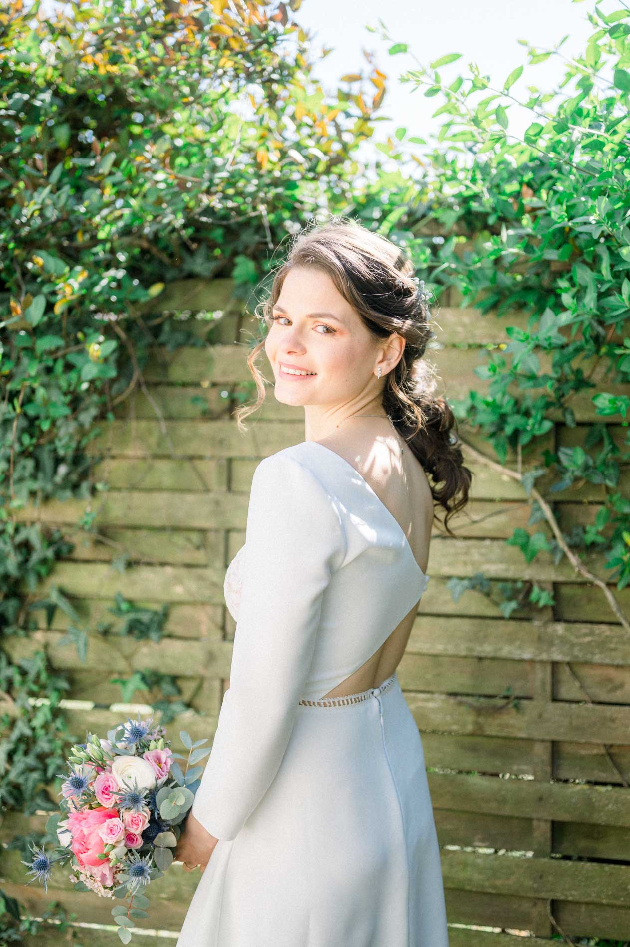 La mariée se retourne en souriant devant une palissade de lierre
