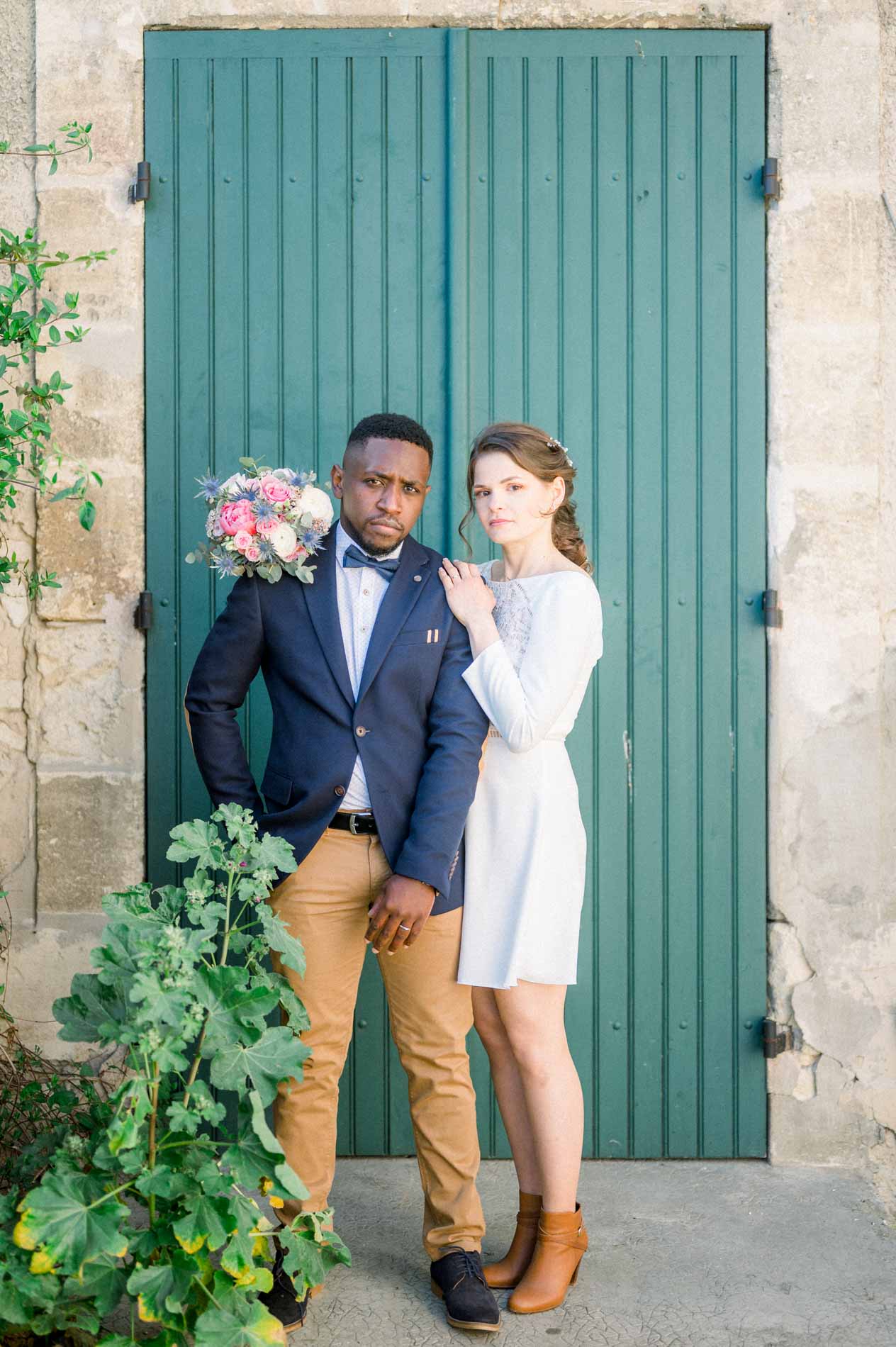 Claire et Mohamed posent devant une porte verte encadrée de pierre et de vigne