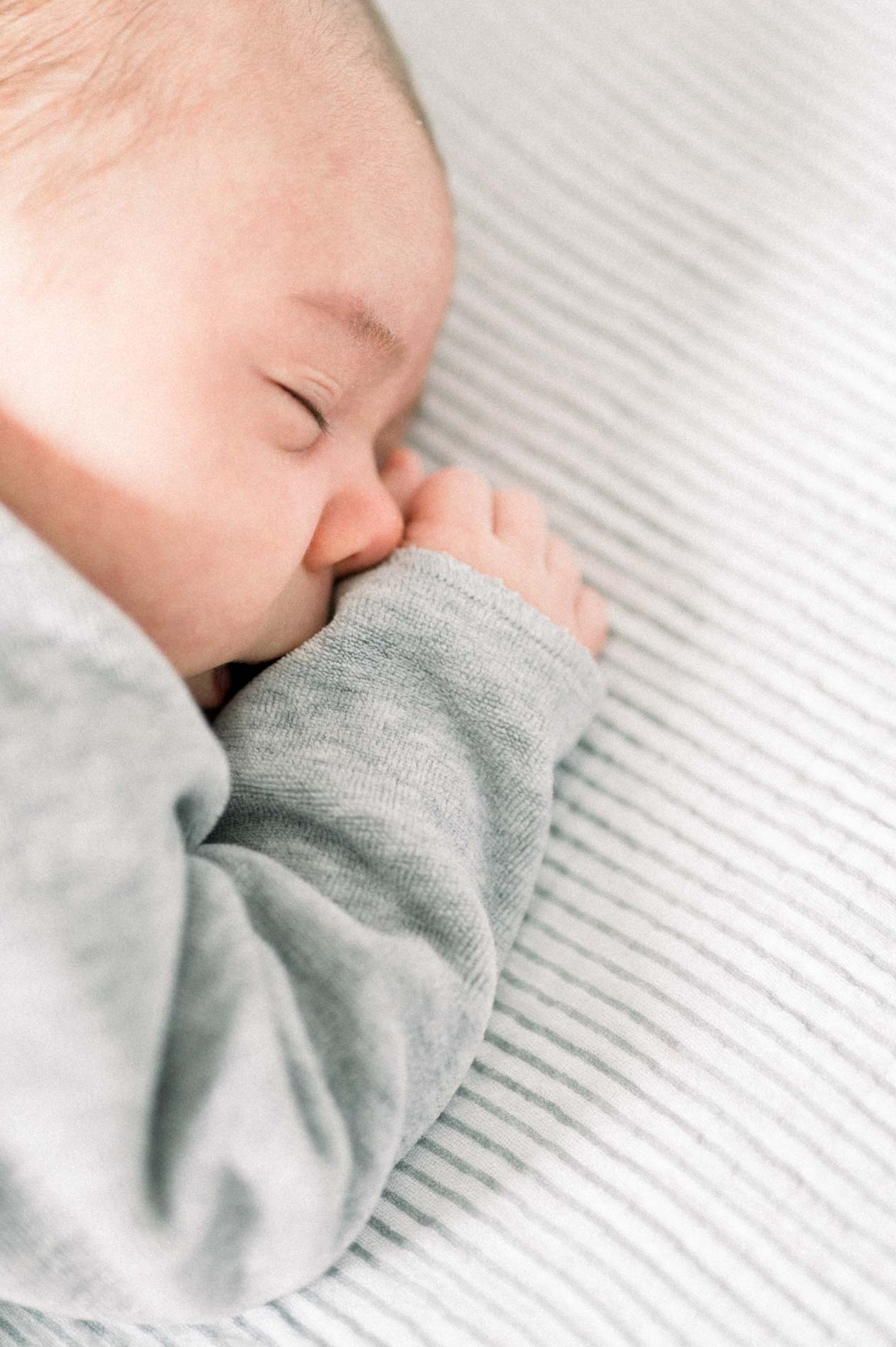 Nouveau-né endormi en pyjama gris, poing contre la joue
