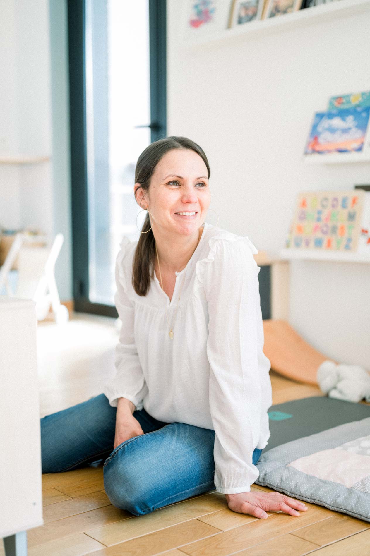 Maman assise par terre dans le salon, souriante, sur un tapis d'éveil