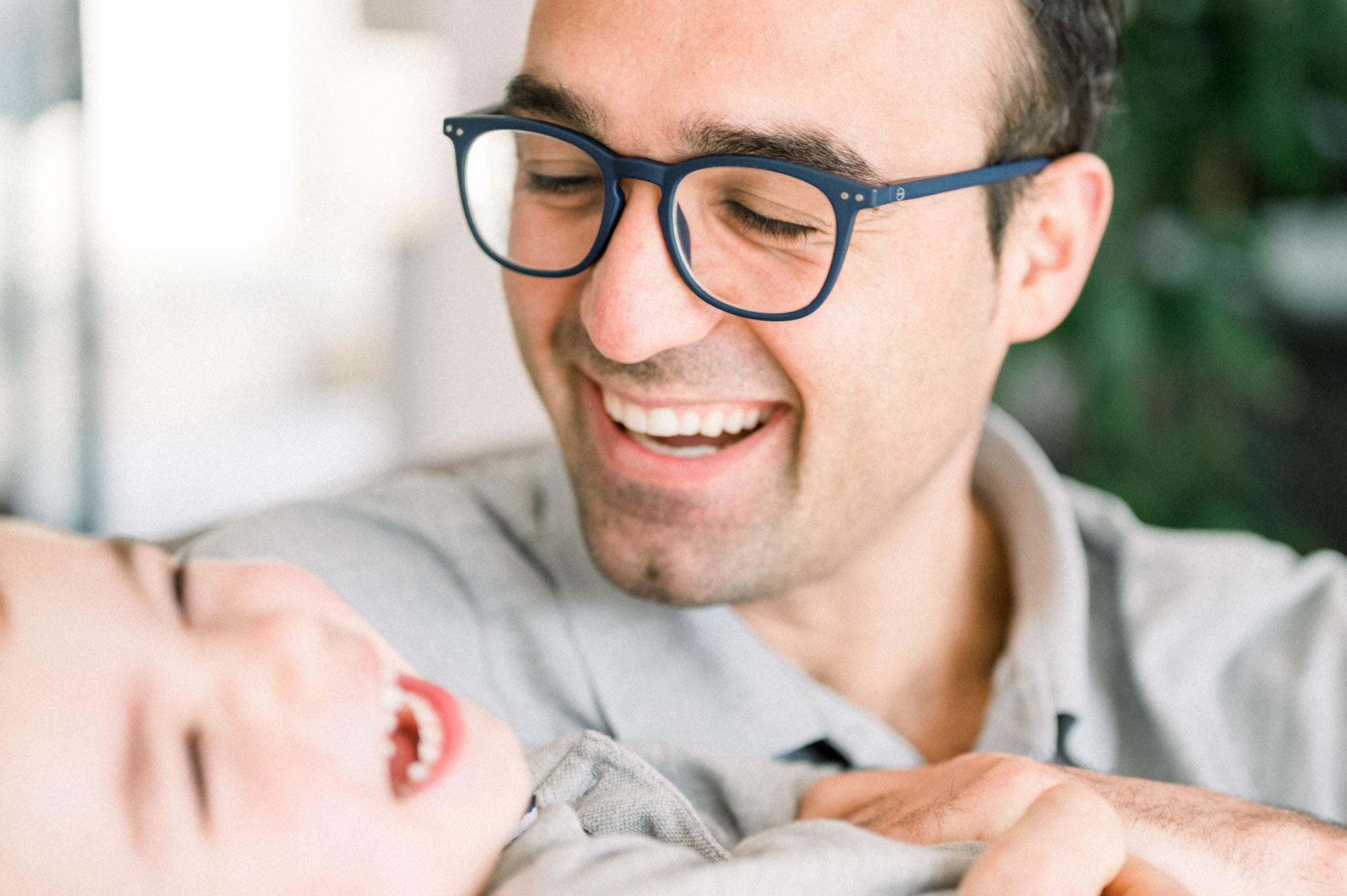 Smiling father in glasses leaning over his baby, at-home lifestyle session