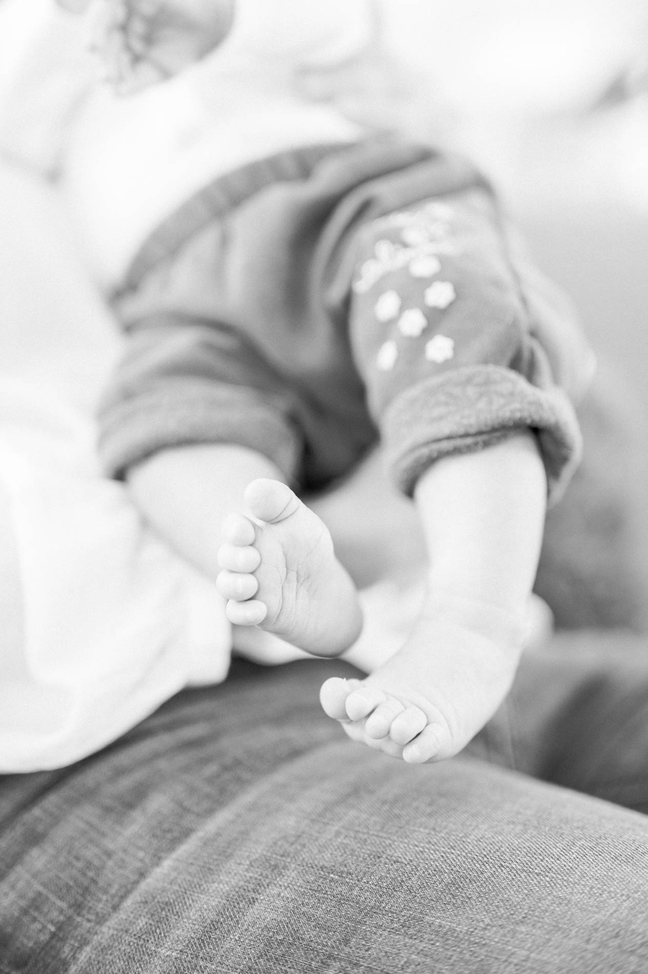 Petits pieds nus de bébé posés sur le jean d'un parent, en noir et blanc