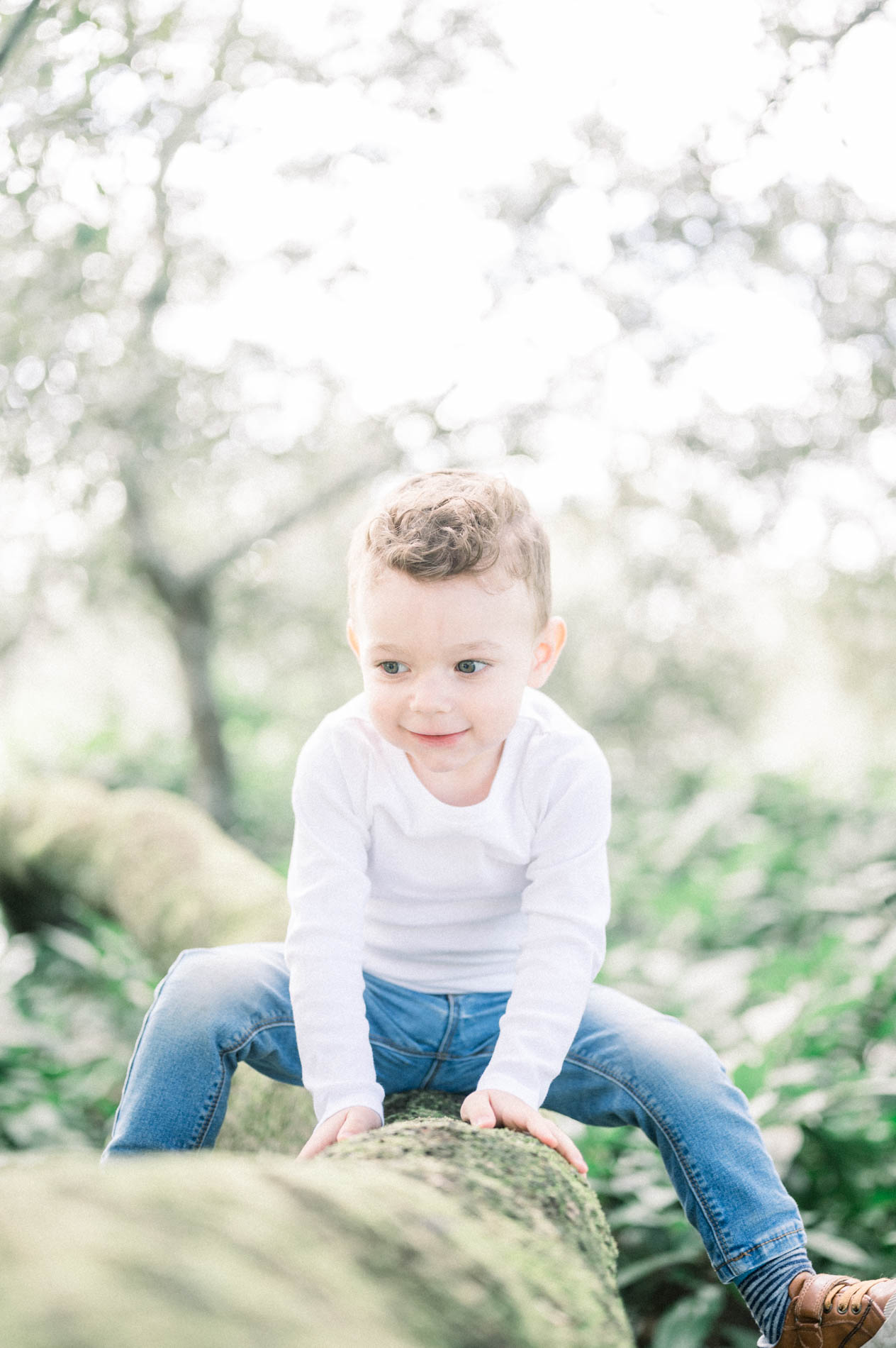 The little boy in a white top climbing onto a tree trunk