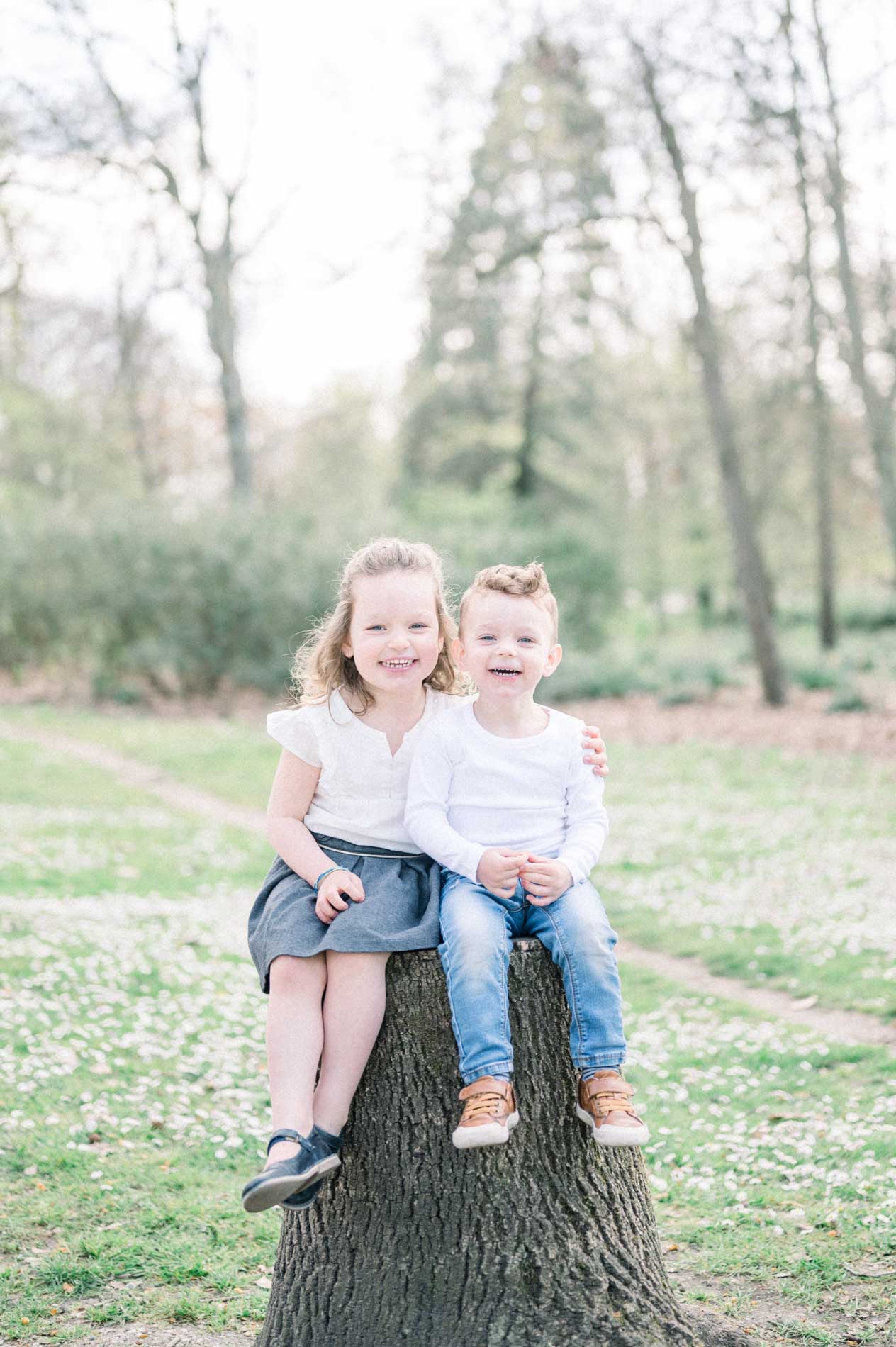 Brother and sister sitting together on a stump in the park meadow