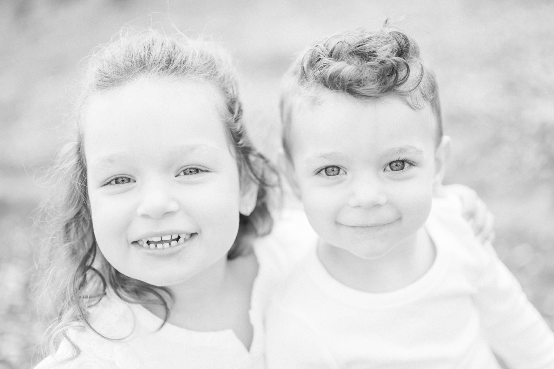 Black and white portrait of a smiling little girl and her younger brother