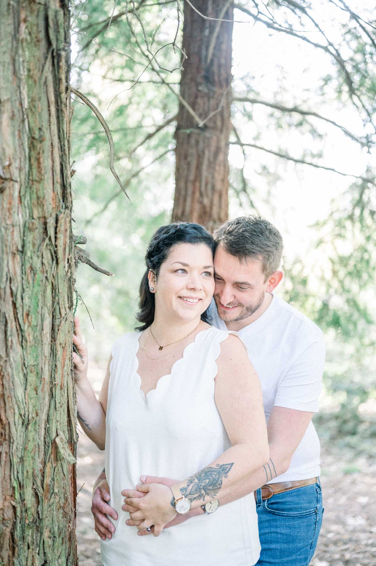 The parents embracing against the red trunk of a redwood